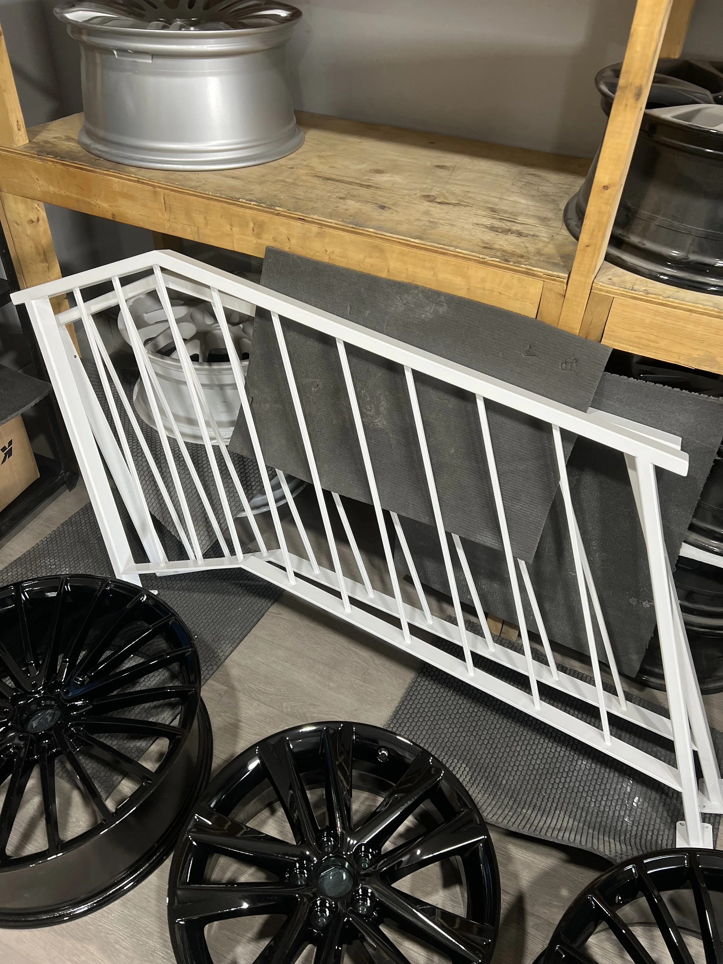 Car wheel rims and a white metal rack with black foam padding leaning against a wooden workbench.