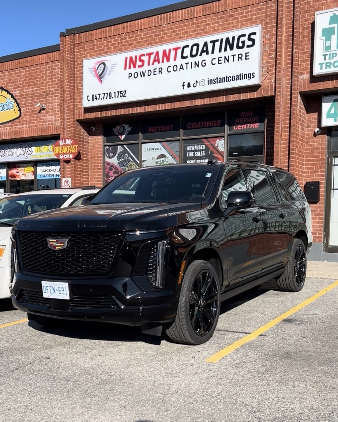Black SUV parked in front of a brick building with a sign for Instant Coatings, a powder coating center.