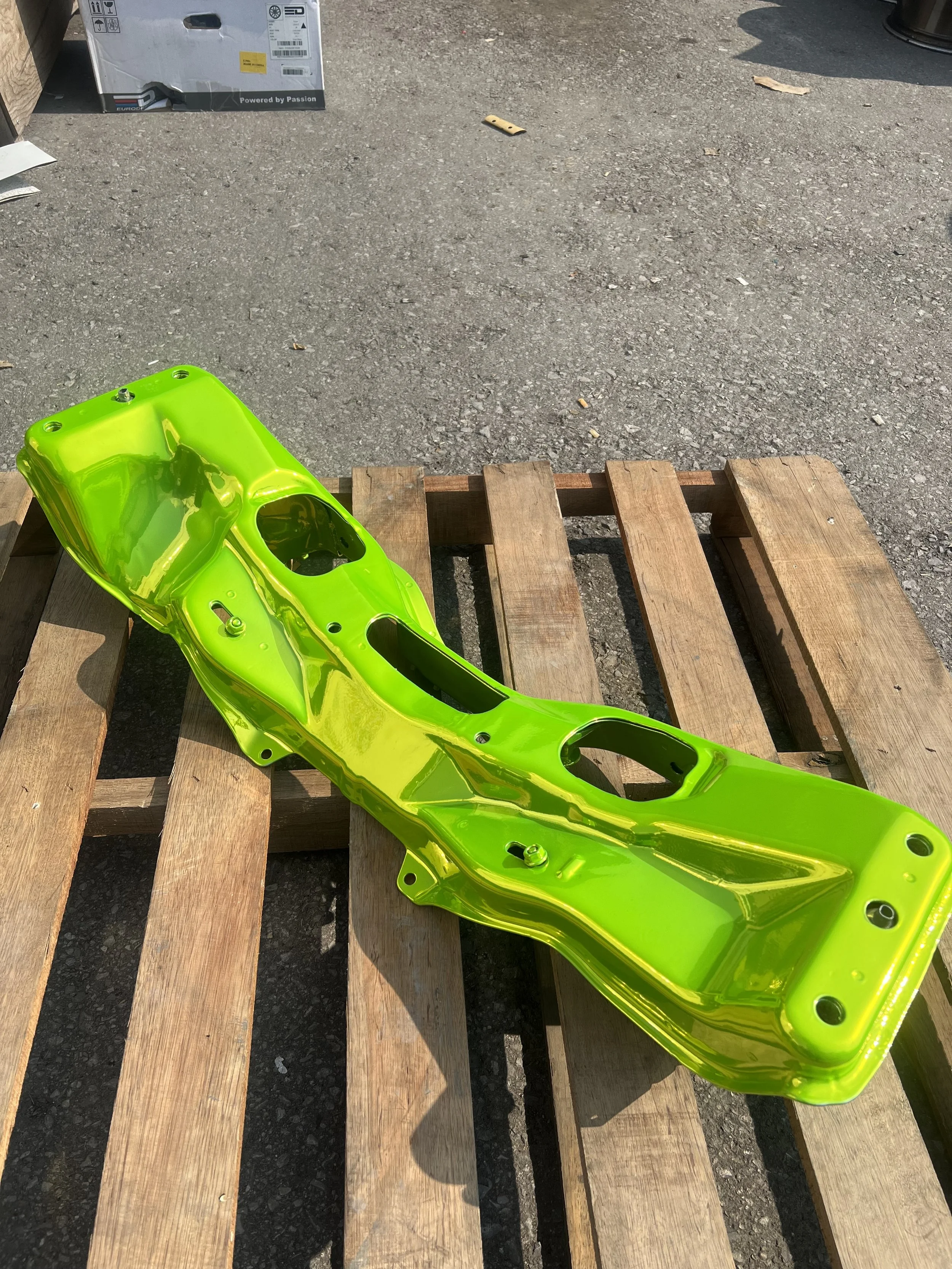 A bright yellow-green motorcycle part, possibly a frame or fairing, resting on a wooden pallet outdoors.