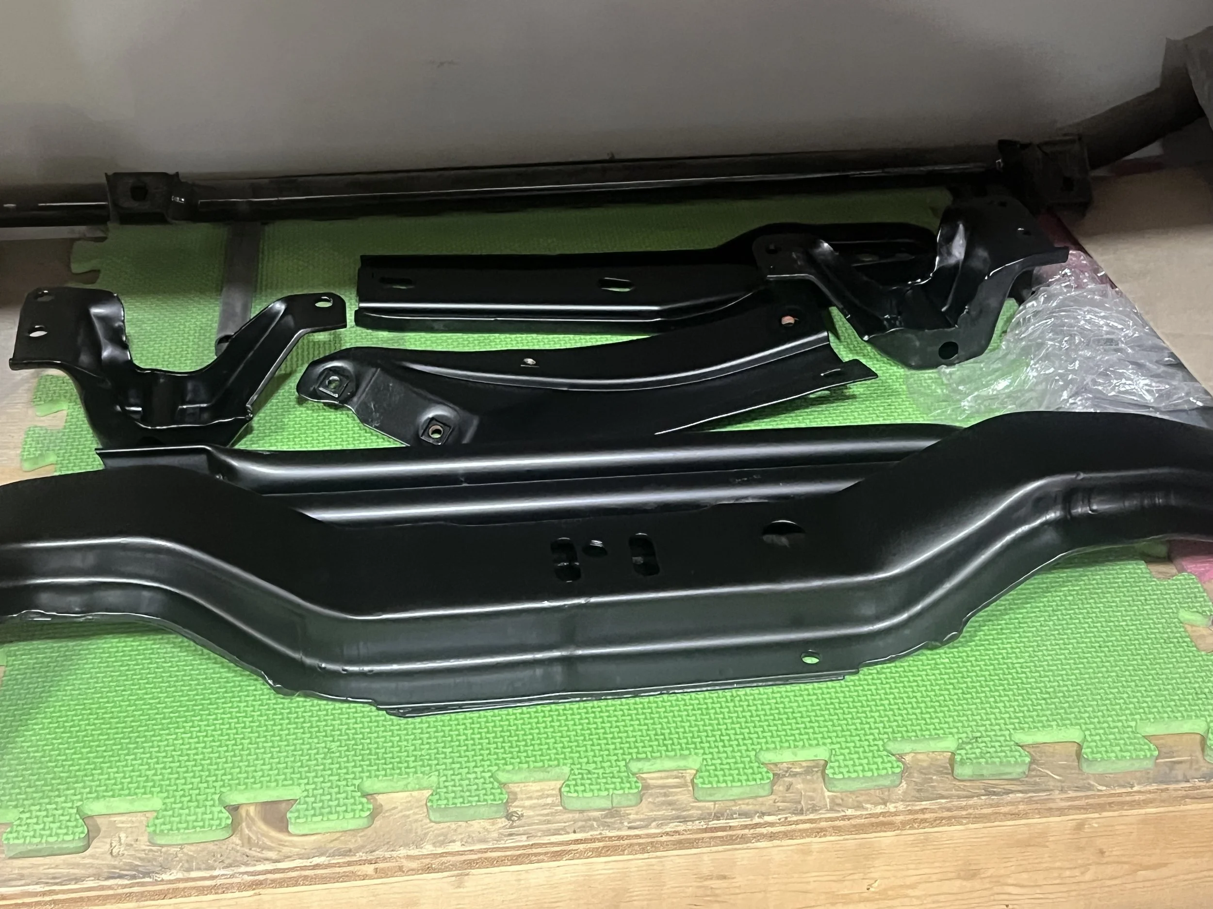 Black metal automotive parts arranged on a green foam mat.