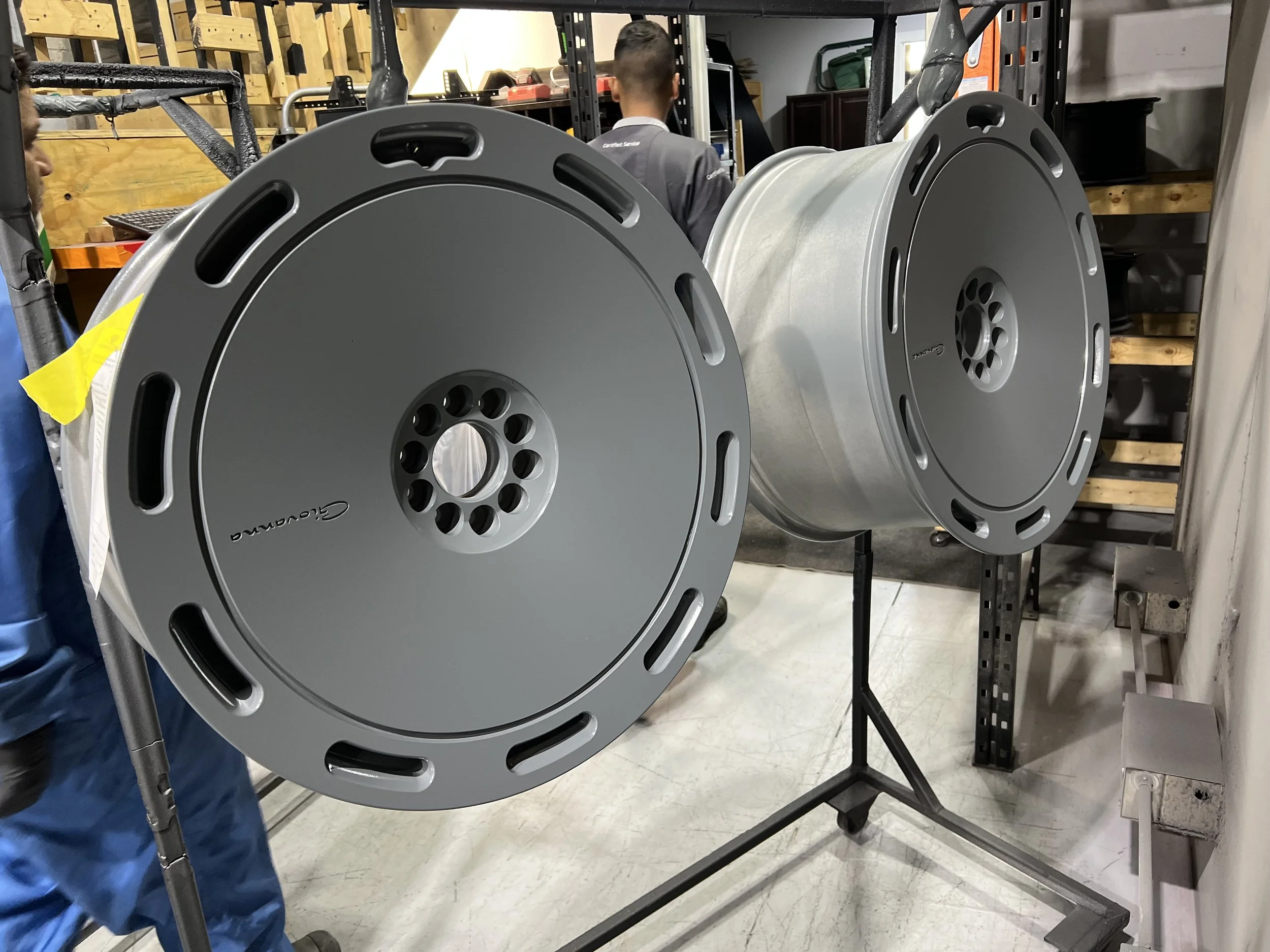 Two large, cylindrical metal drums with honeycomb-patterned holes on one end, mounted on a display stand in a workshop or storage area.