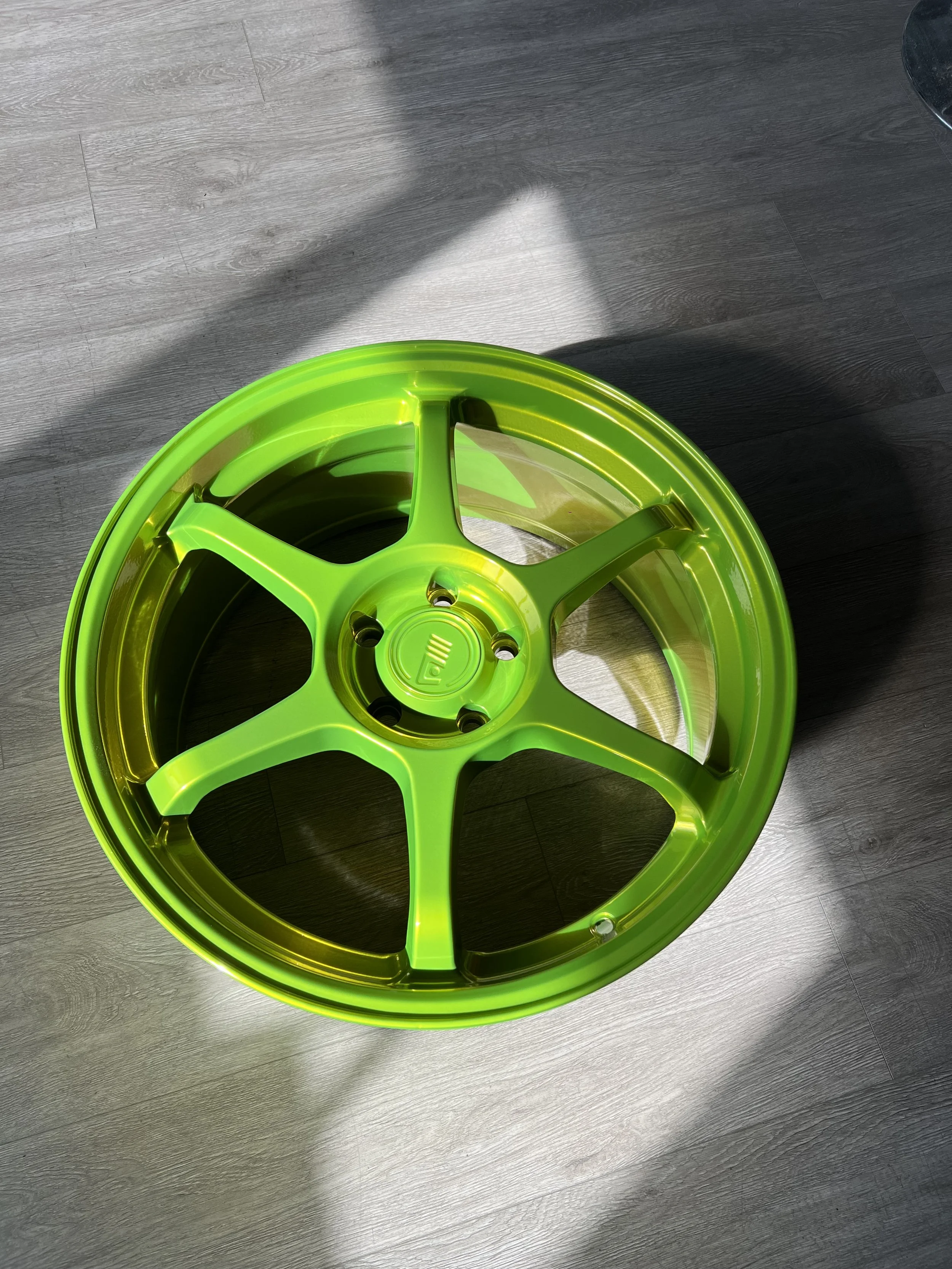 Bright green, multi-spoke alloy wheel rim on a wood floor.