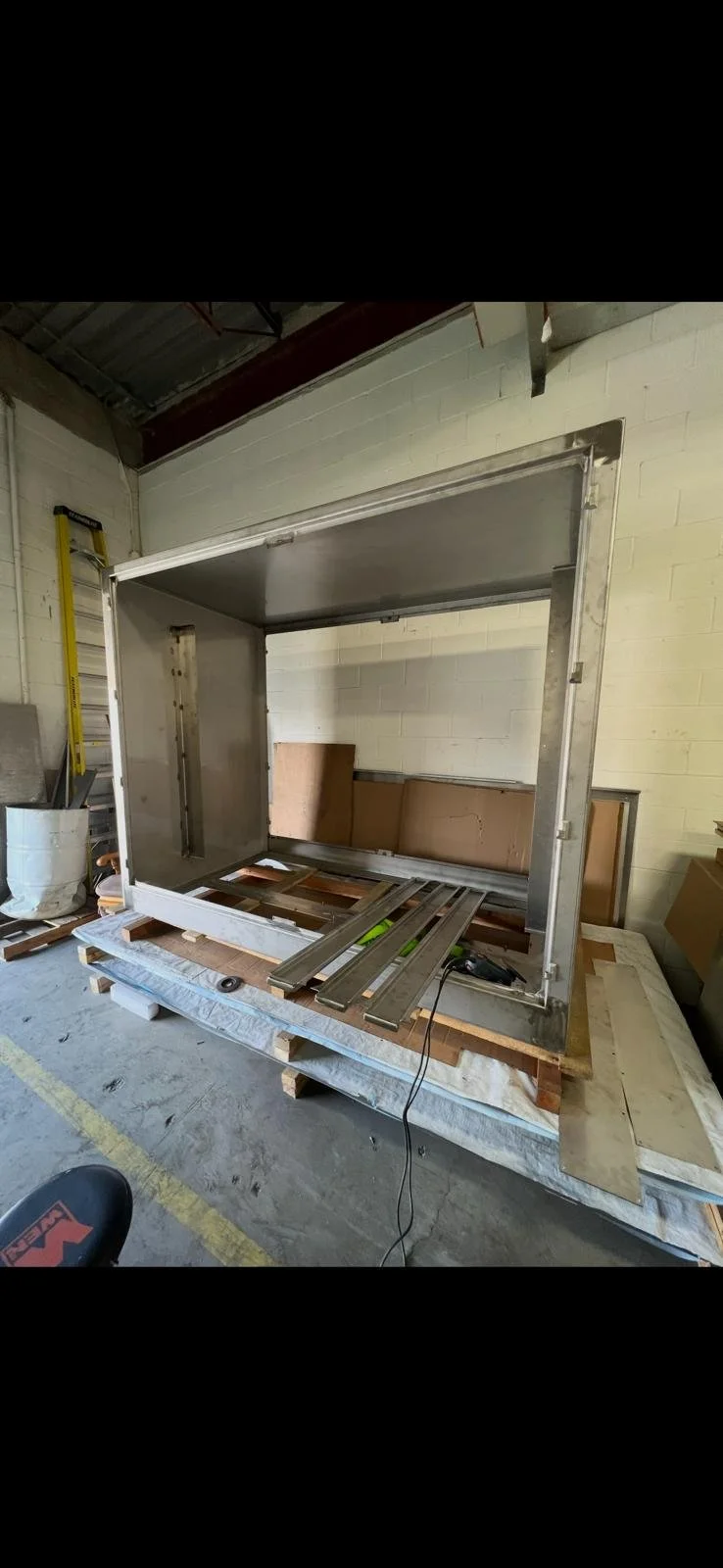 Metal structure being assembled on wooden pallets inside a warehouse.