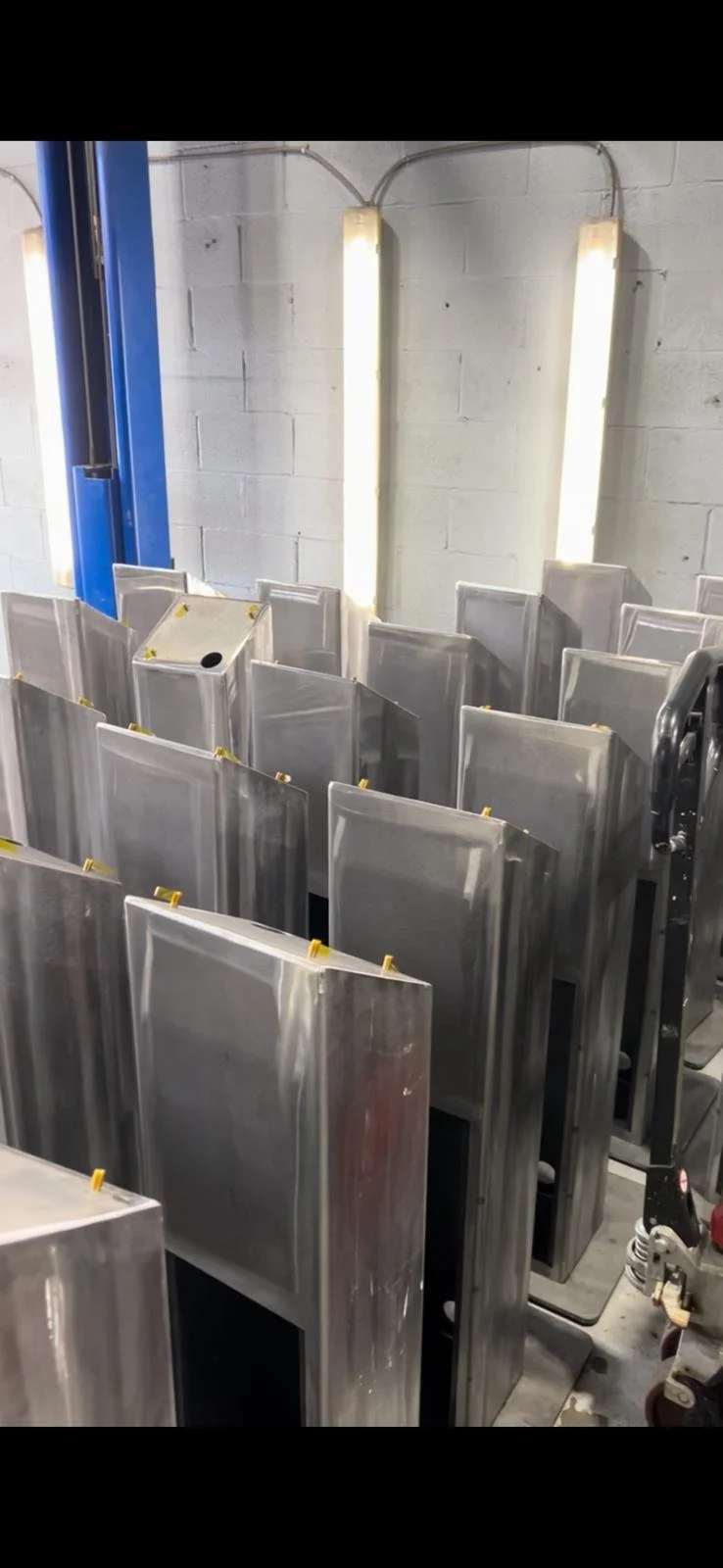 Several stainless steel or metal booths or lockers arranged in rows in an industrial or manufacturing setting with fluorescent lighting on a concrete wall.