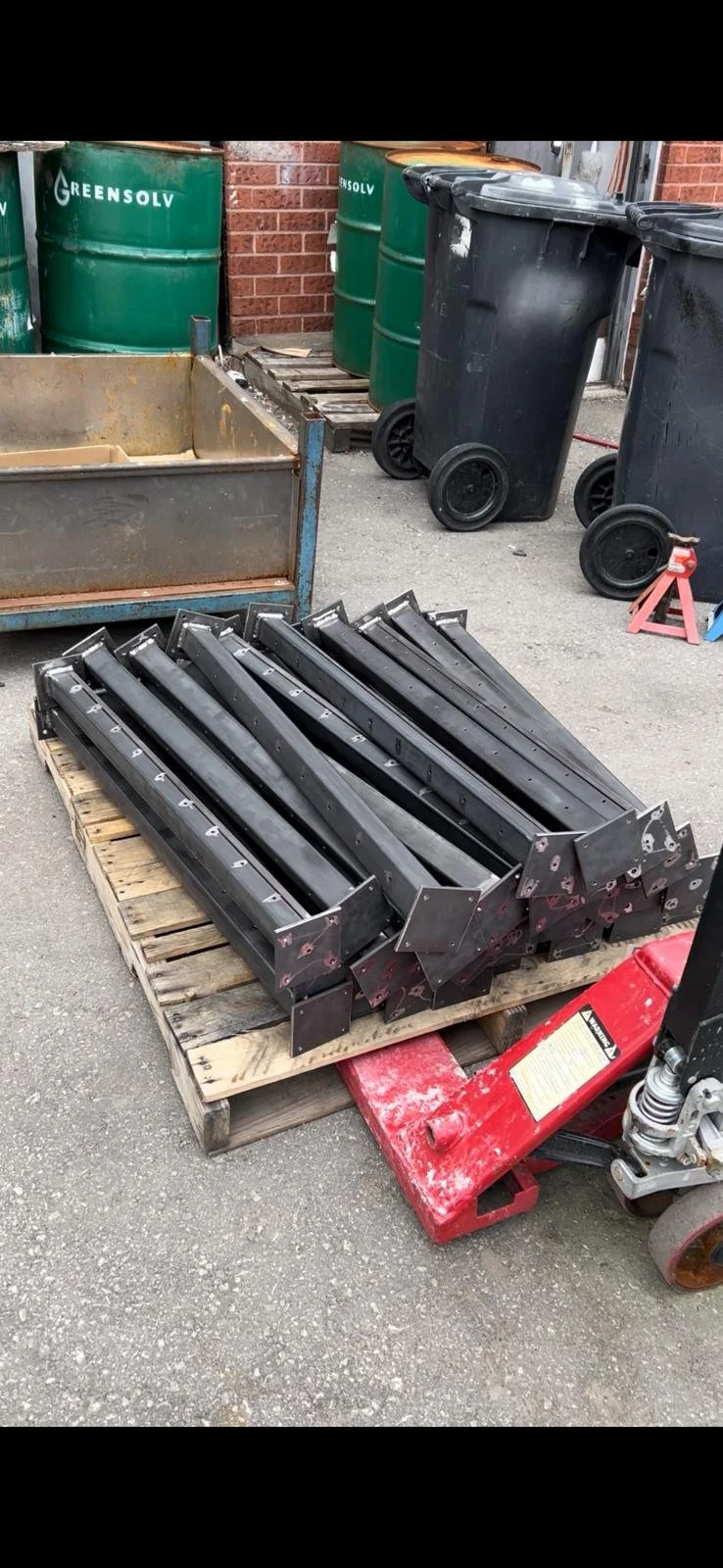 Metal ramps placed on a wooden pallet outdoors near trash bins and green barrels.