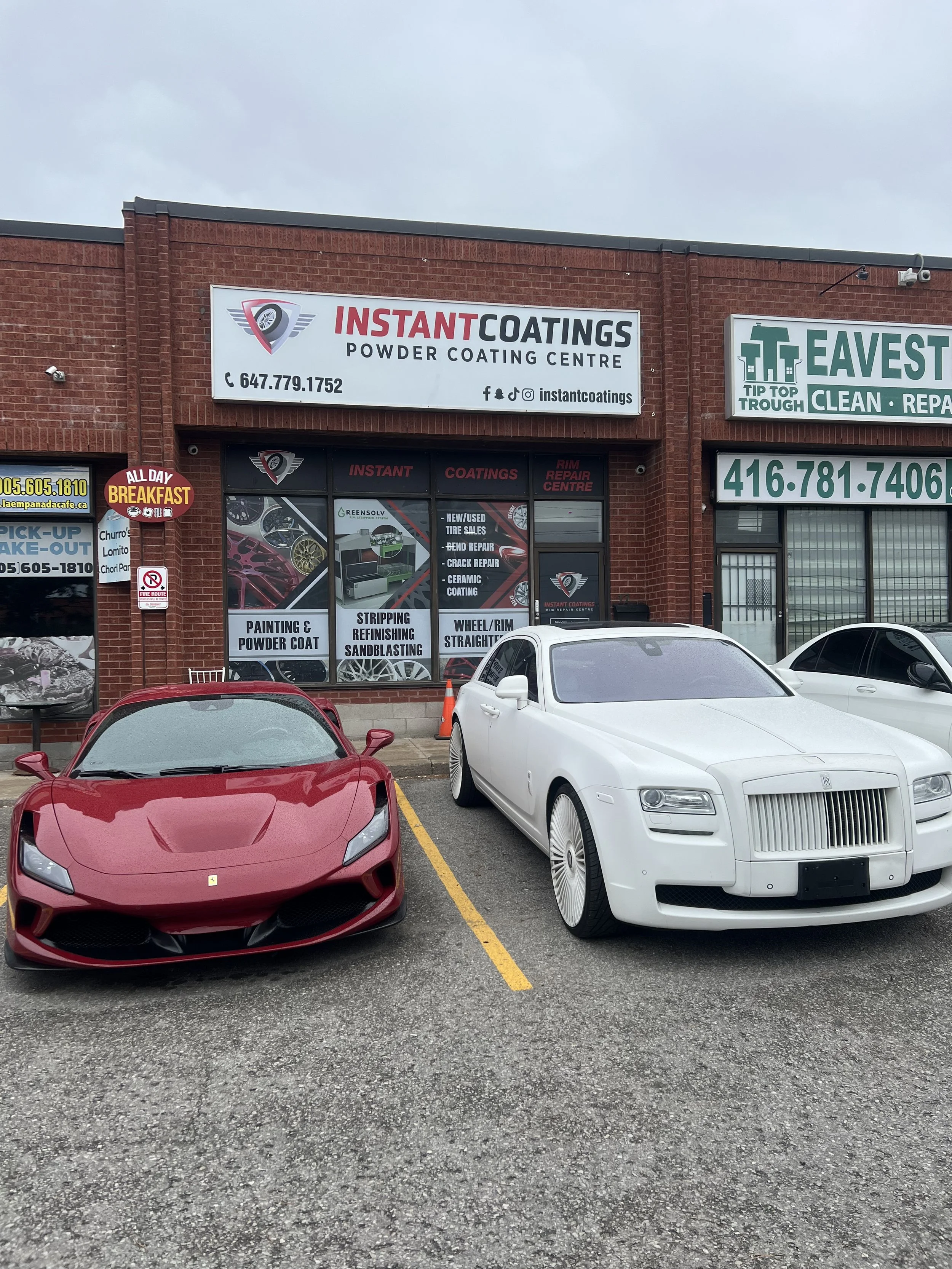 Red sports car and white luxury car parked outside a coating business in front of a red brick building.