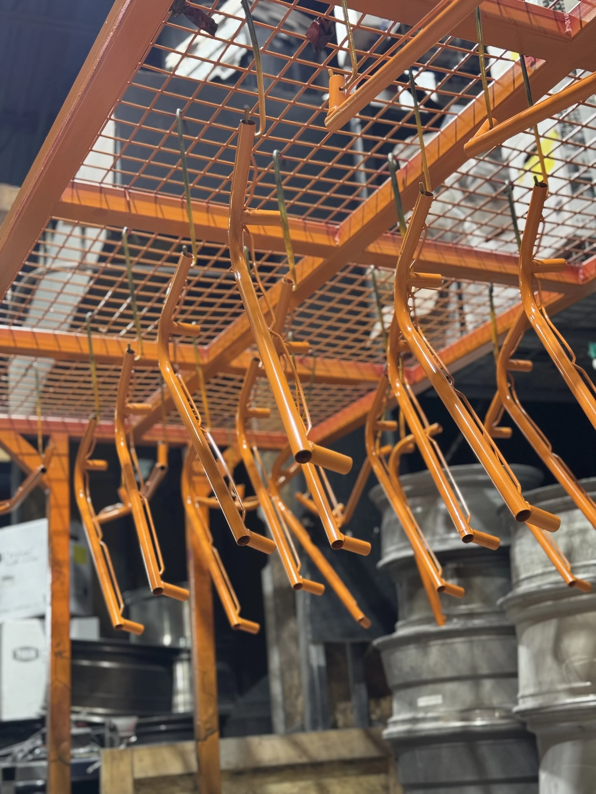 Orange wire shelving unit with metal hooks hanging from the bottom, in a hardware or industrial store.