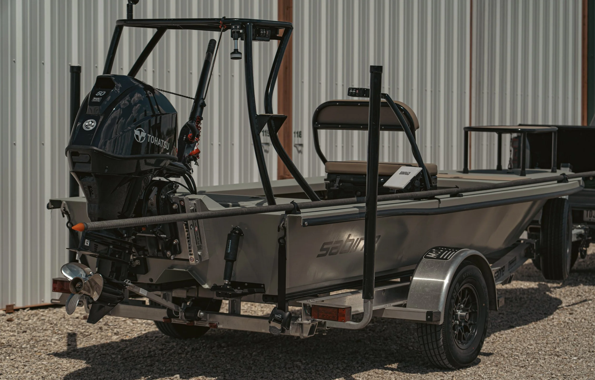 A boat on a trailer with an outboard motor, parked outside against a metal building wall.
