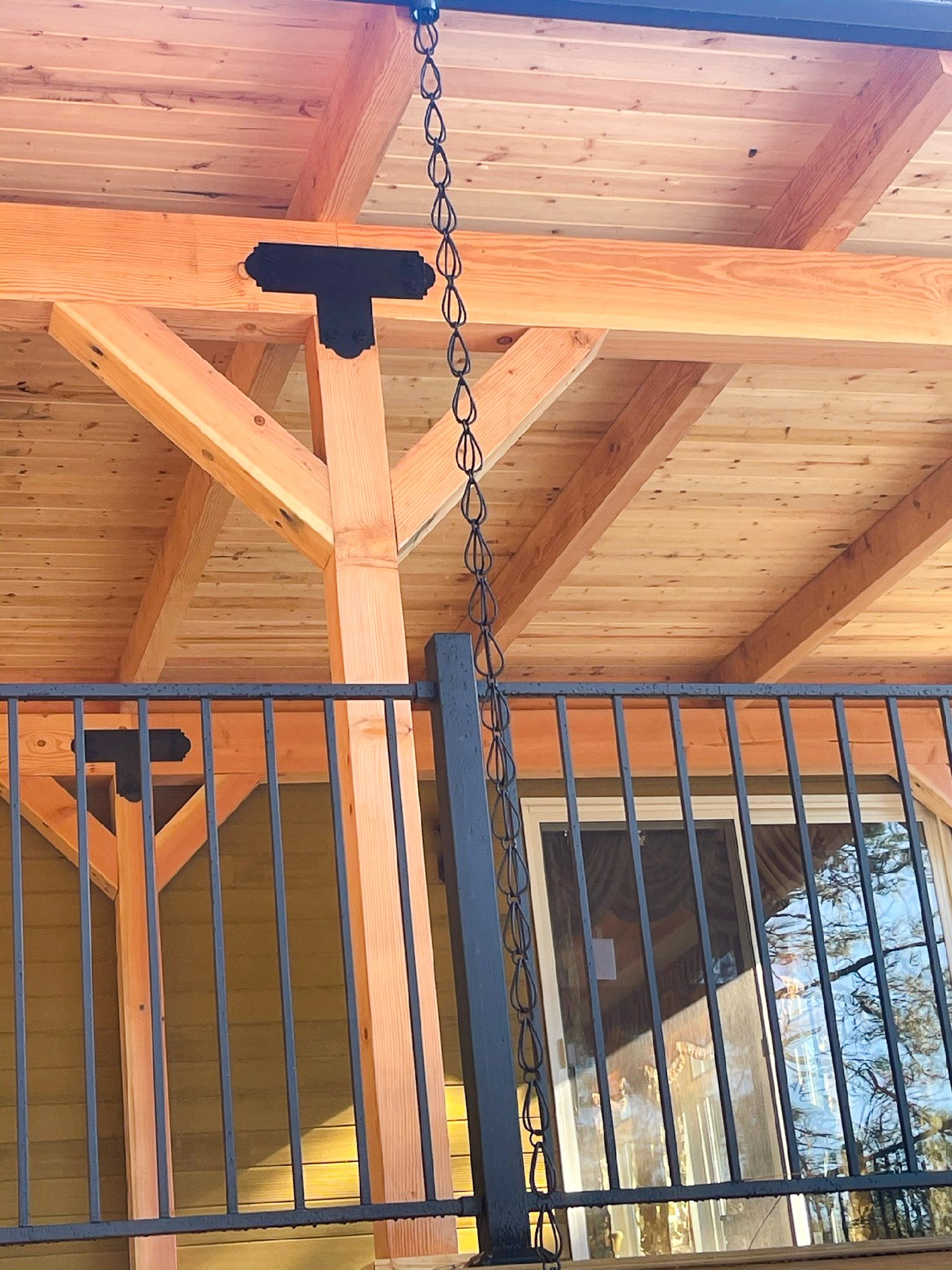 Close-up view of a wooden porch roof with a chain hanging from it and a black metal railing in front.