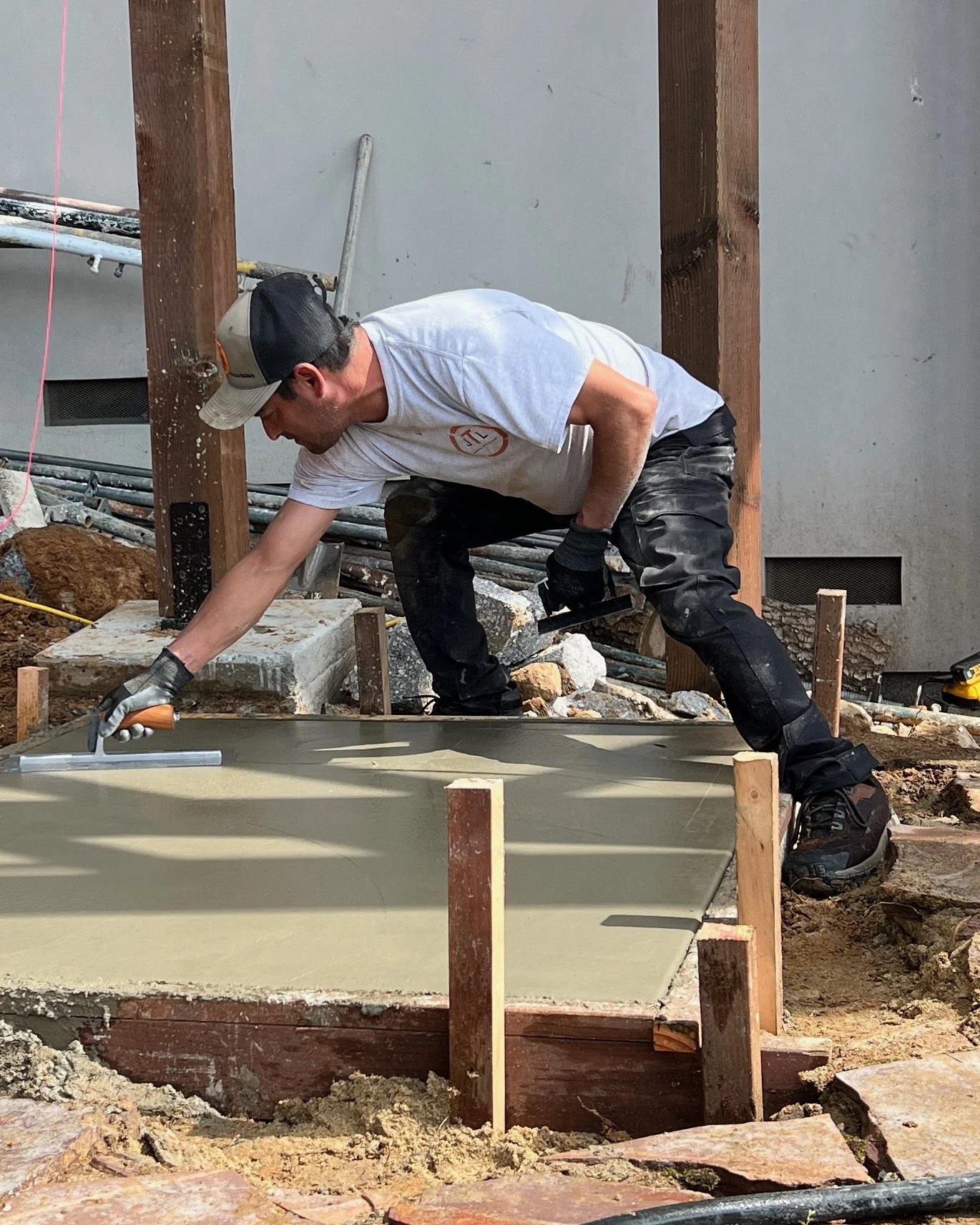 A construction worker smoothing wet concrete with a trowel at a building site.