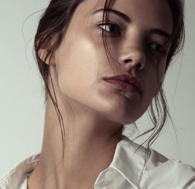 Close-up of a woman with light skin and brown hair looking slightly away, wearing a white shirt.