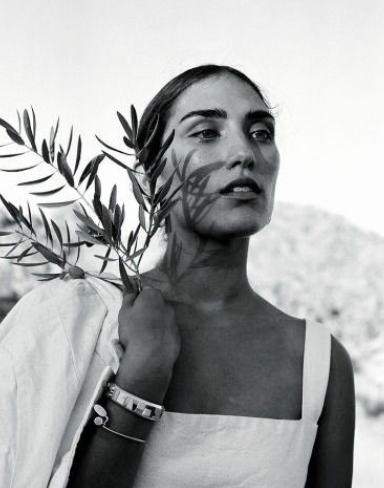 Black and white photo of a woman holding a branch with leaves near her face, looking into the distance.