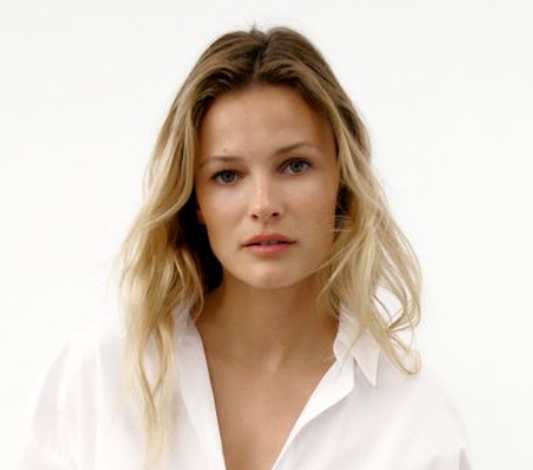 A young woman with blonde hair wearing a white shirt against a plain white background.