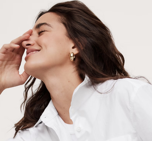 A woman smiling with eyes closed, touching her forehead.