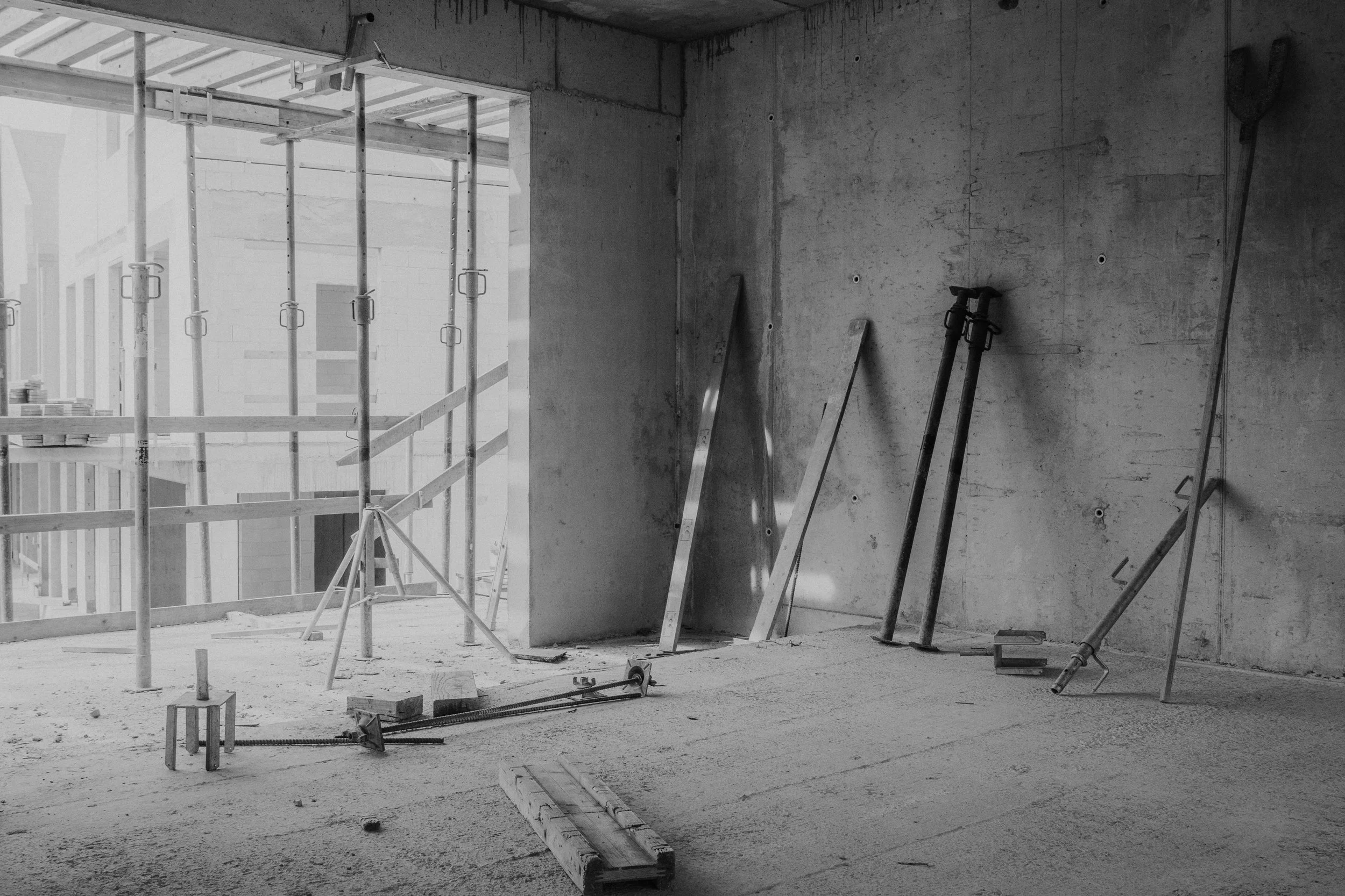 Interior of a construction site with scaffolding, tools, and building materials on the floor.