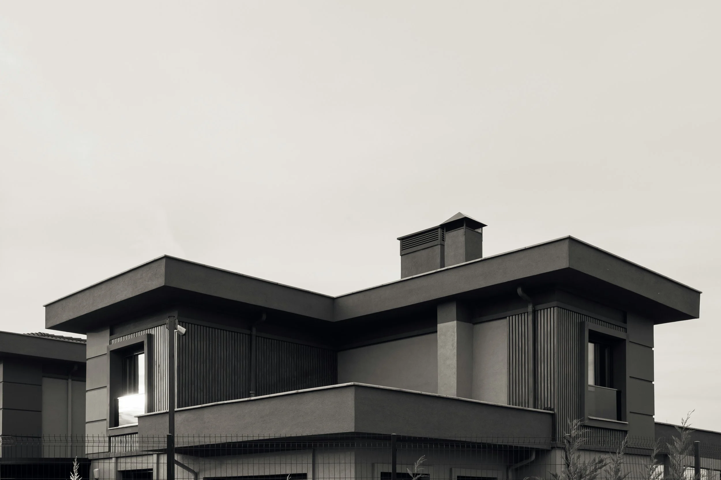 Black and gray modern two-story house with flat roof and large windows, exterior view against a cloudy sky.