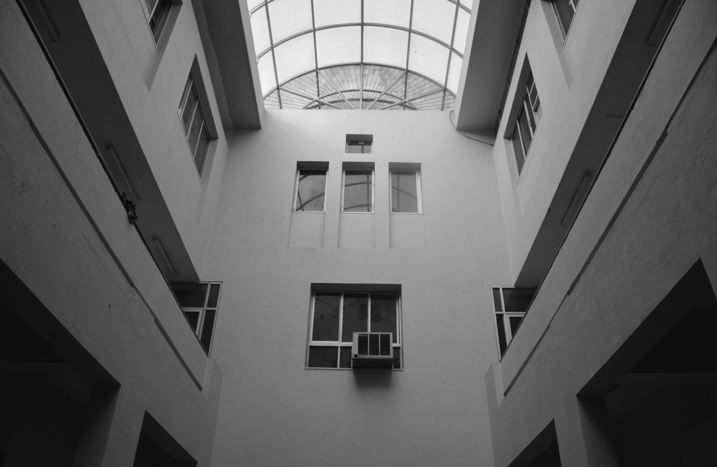Black and white photo of the interior courtyard of a multi-story building, looking up towards the glass roof.