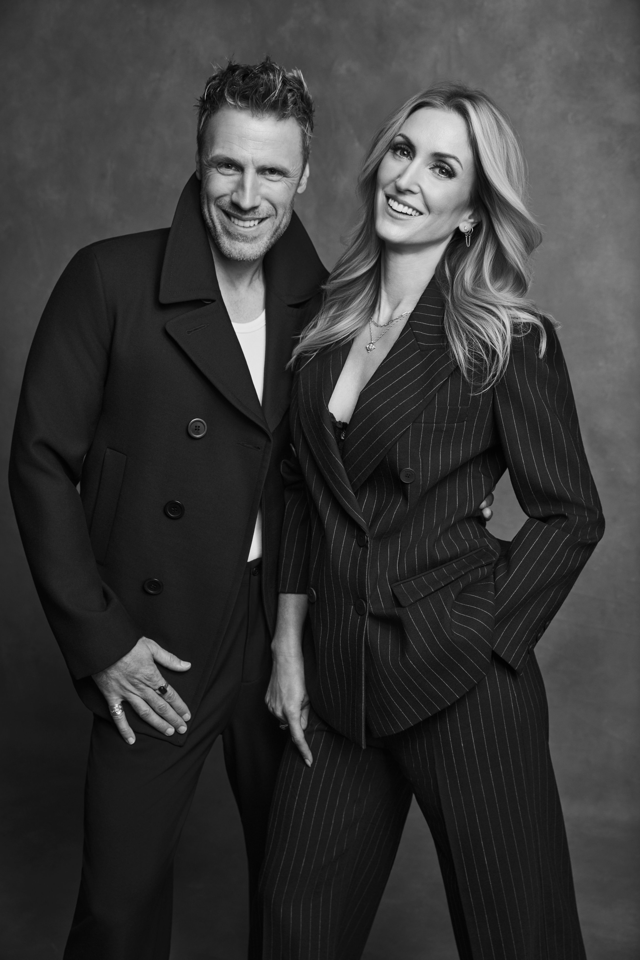 Black and white photo of a man and a woman posing together, both wearing business suits, smiling, with a textured background.