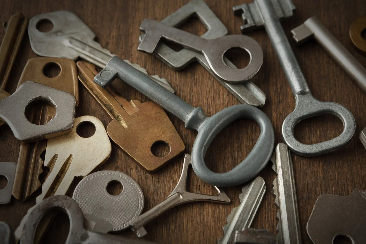 A collection of various metal keys of different shapes, sizes, and finishes scattered on a wooden surface.