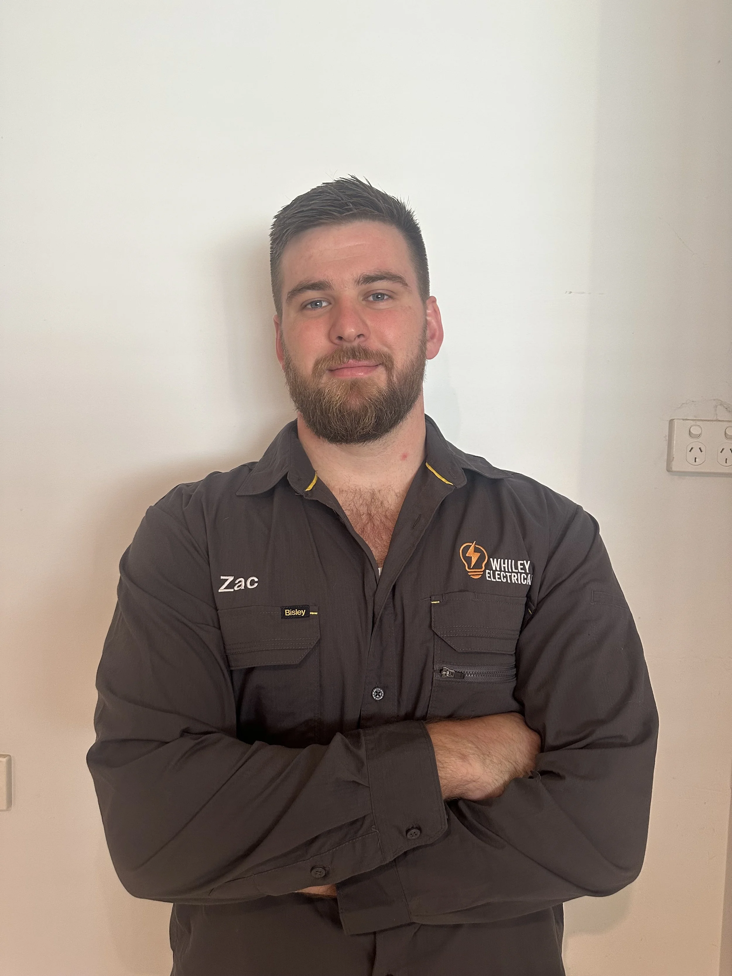 A man with a beard smiling at the camera with his arms crossed. - Zac Whiley - Bendigo Electrician - About