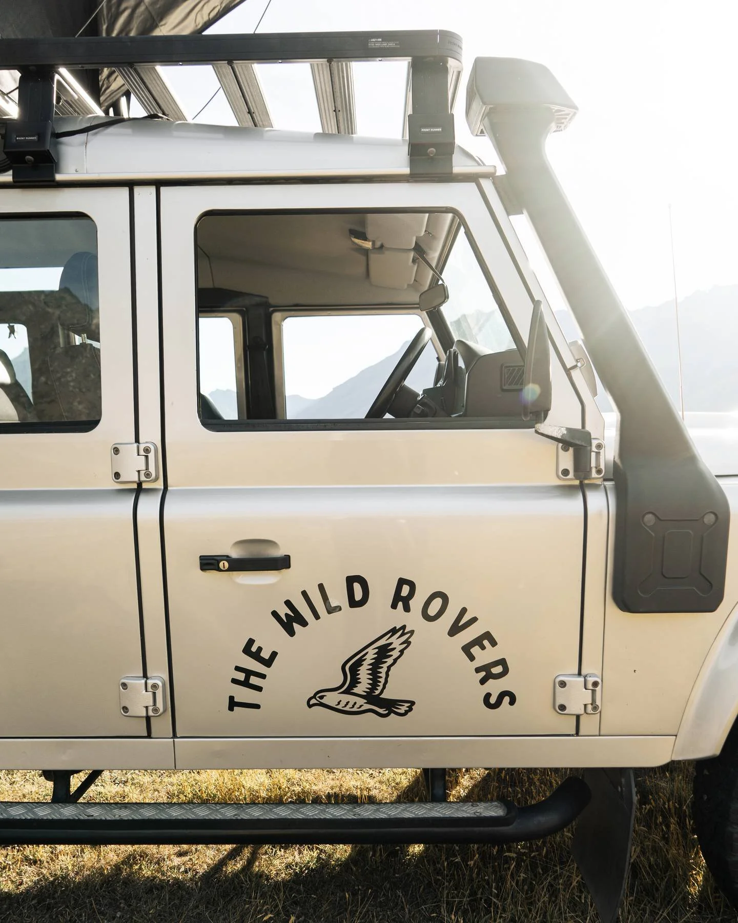 Close-up of a white off-road vehicle with a logo of a bird and the text "The Wild Rovers" on the door, showing part of the interior and exterior details.