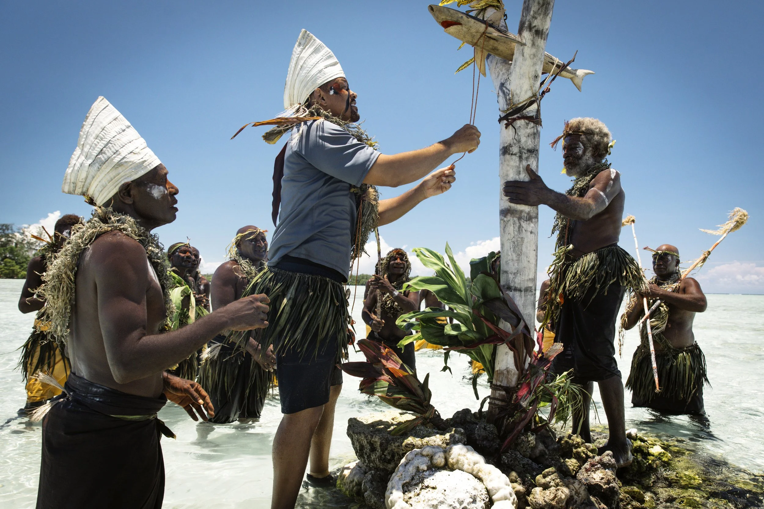Will Smith & People in the South Pacific Island conducting a traditional ceremony on a beach, involving a decorated pole and natural elements.