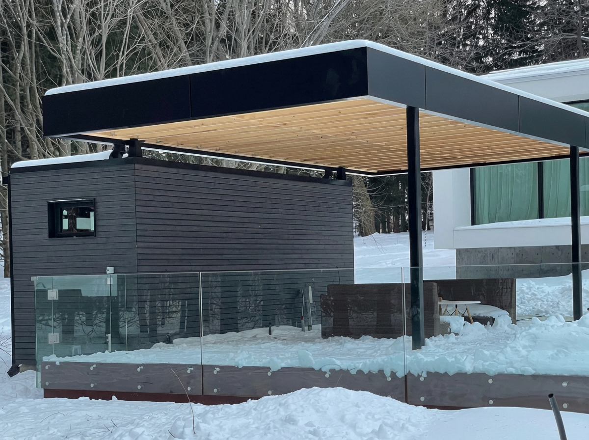 Modern house with large glass windows and a wooden and metal exterior, set in a snowy landscape with trees in the background.