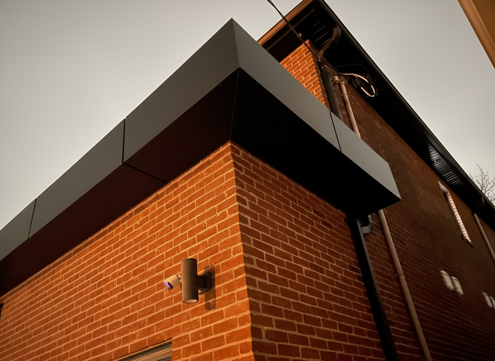 Modern two-story house with gray and red exterior, large front windows, concrete steps, and a snowy yard with trees and a chain-link fence on the left.