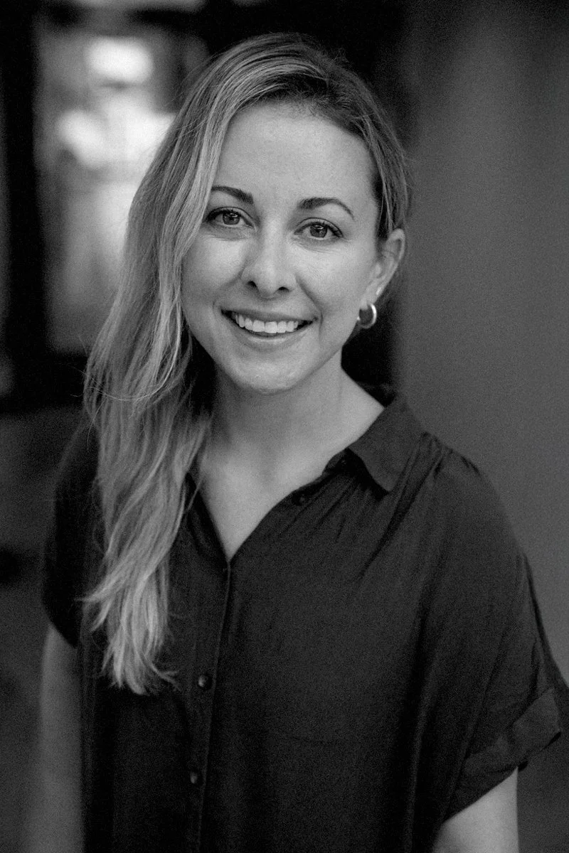 Black and white portrait of a woman with long, wavy hair, smiling, wearing a dark collared shirt and hoop earrings.