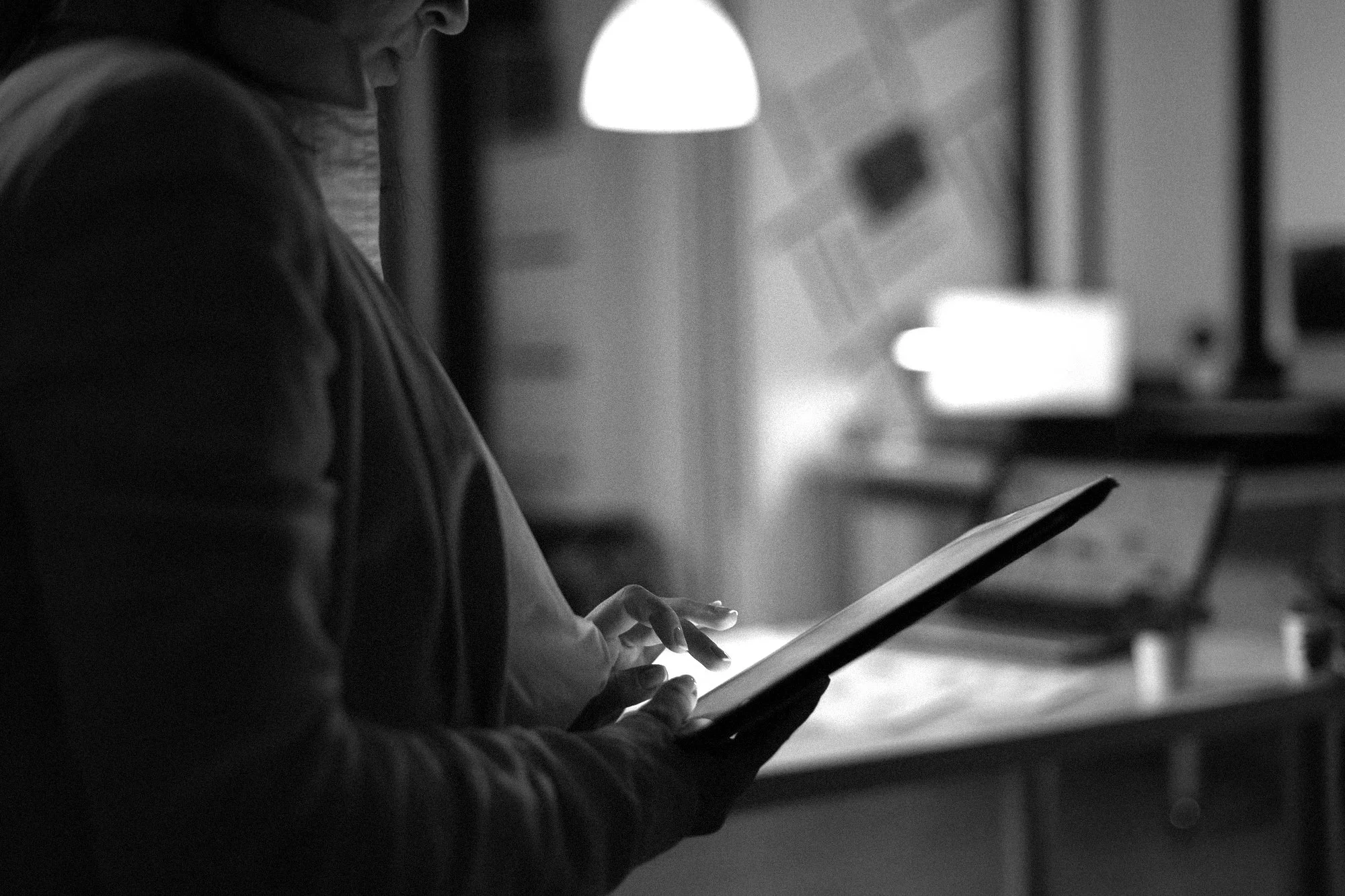 Person using a tablet computer in a dimly lit room with hanging lights and a blurred background.