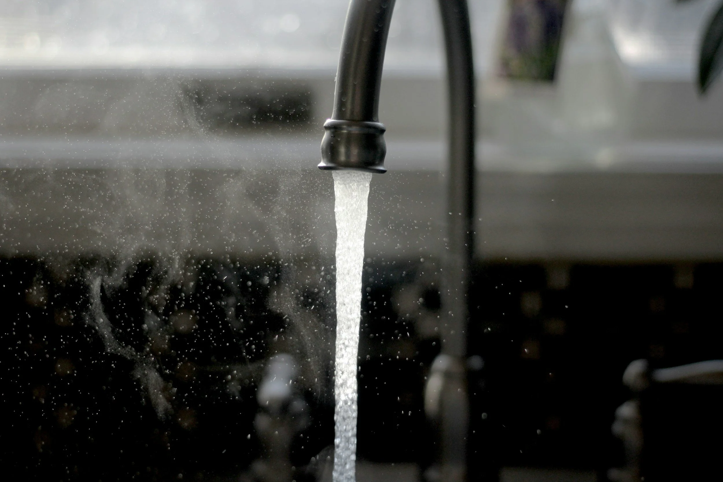 Close-up of water flowing from a tap onto a dark surface, with water droplets splashing and scattering around.