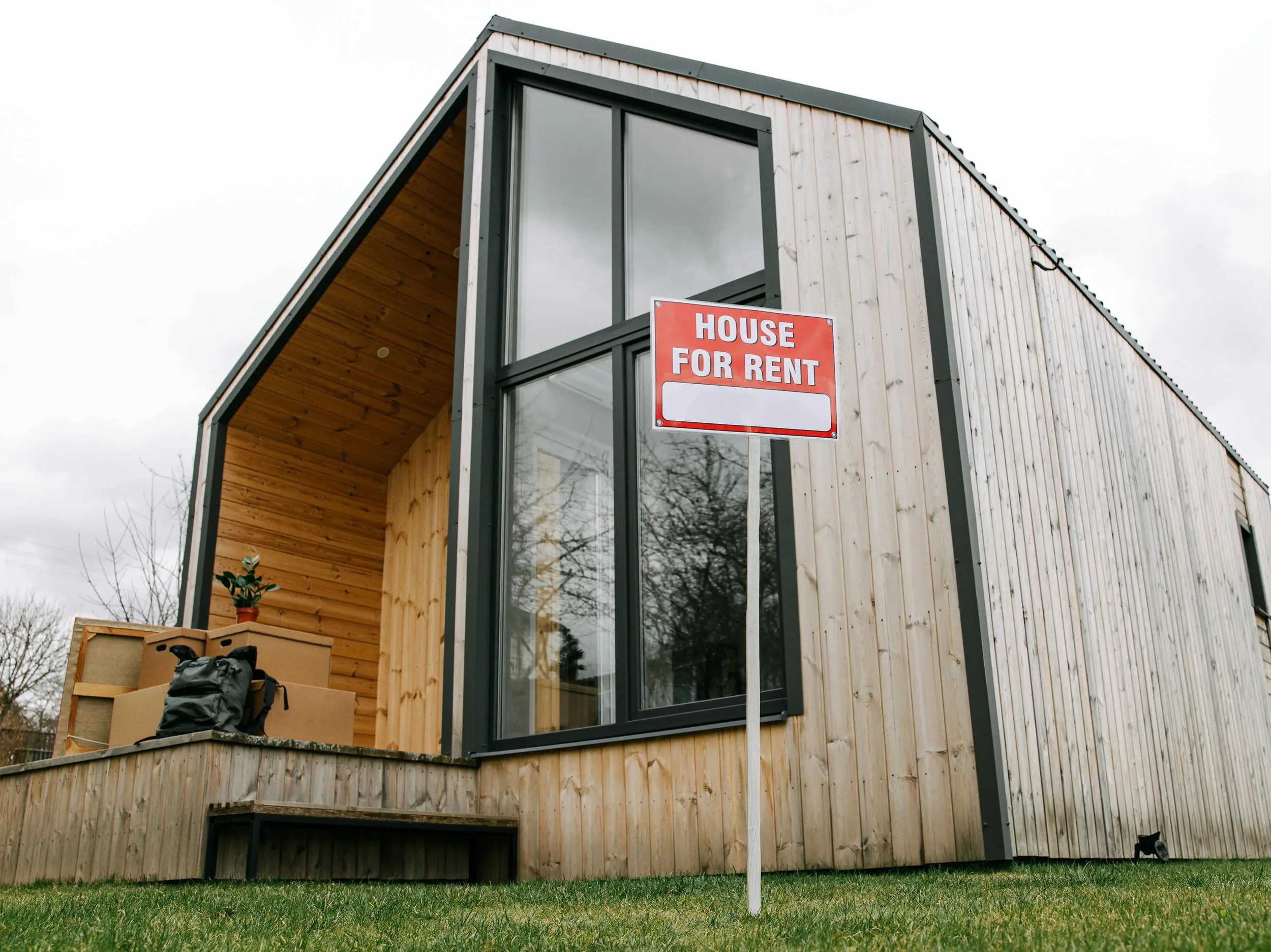 Modern two-story wooden house with large windows and a sign that says 'House for Rent' in front.