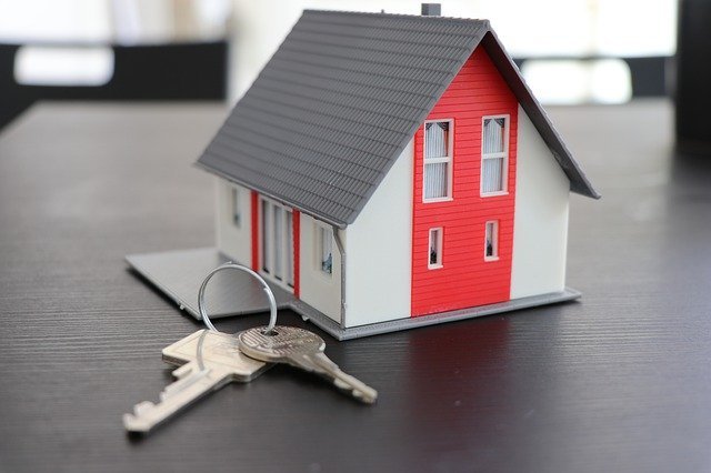 Model house with red siding and keys on a table, representing homeownership and the residential real estate market.