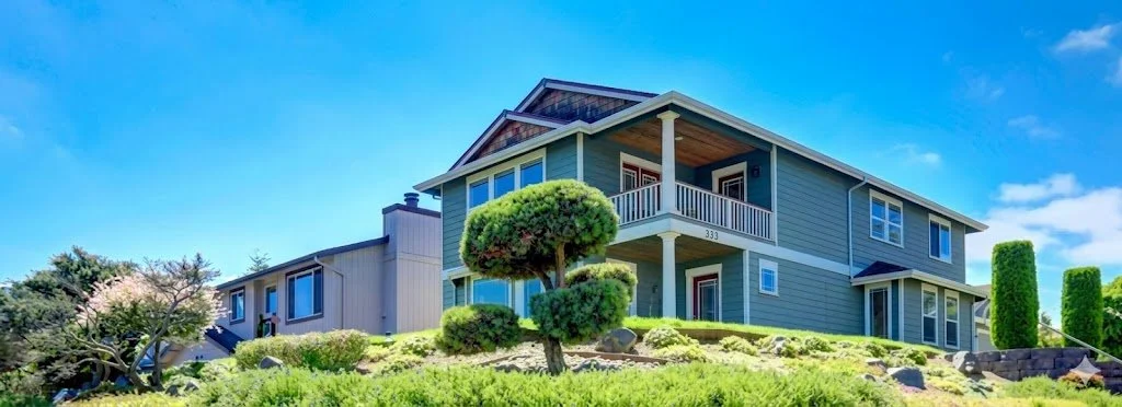 Modern multi-level rental home with landscaped yard and balcony under a bright blue sky