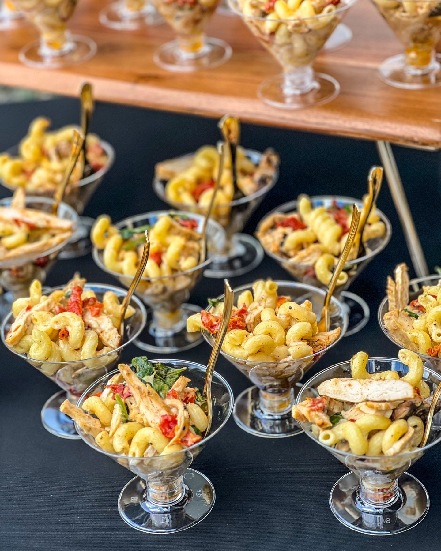 Individual serving cups of macaroni salad with shredded chicken and red bell peppers on a black table.