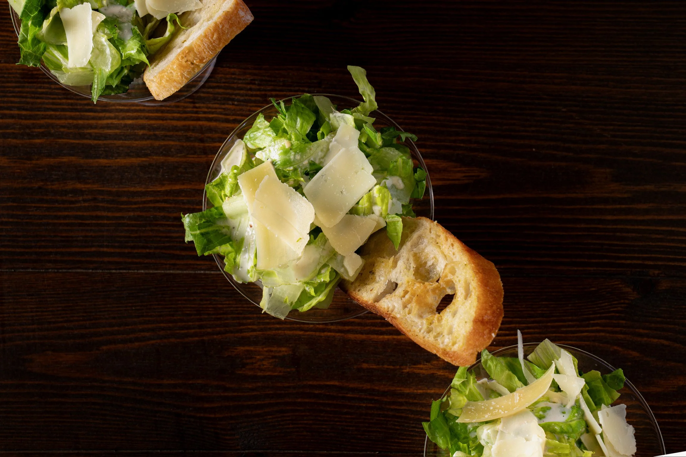 Salad with lettuce, cheese, and croutons in a glass bowl, on a dark wooden table.