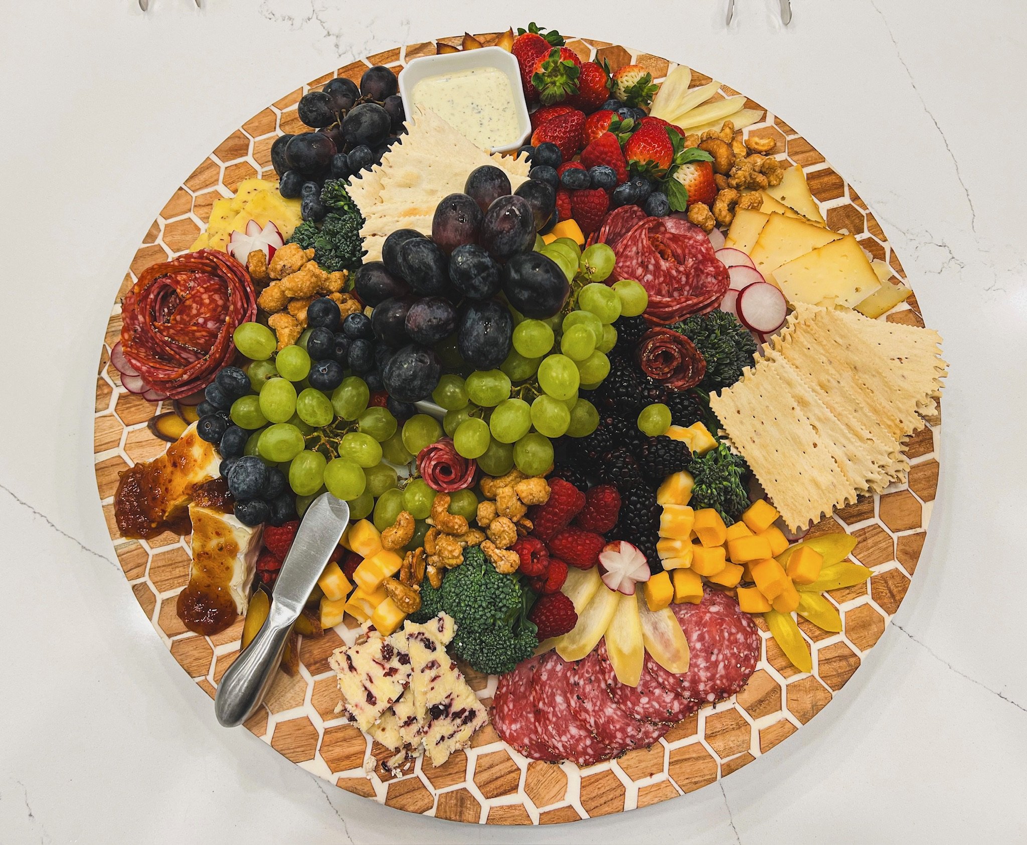 Assorted fresh berries on a wooden tray, including strawberries, kiwi, blueberries, red and green grapes, and dragon fruit.