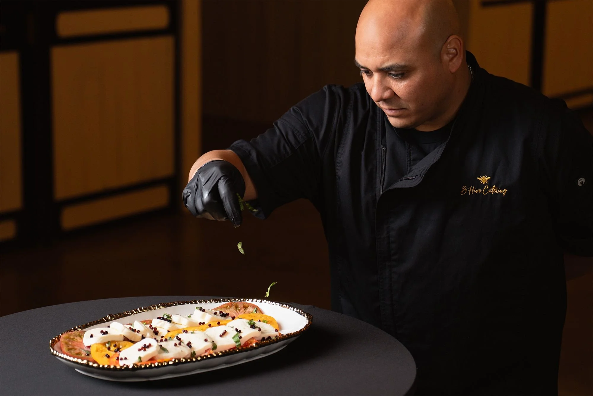 Chef garnishing a plate of salads with herbs and pepper.