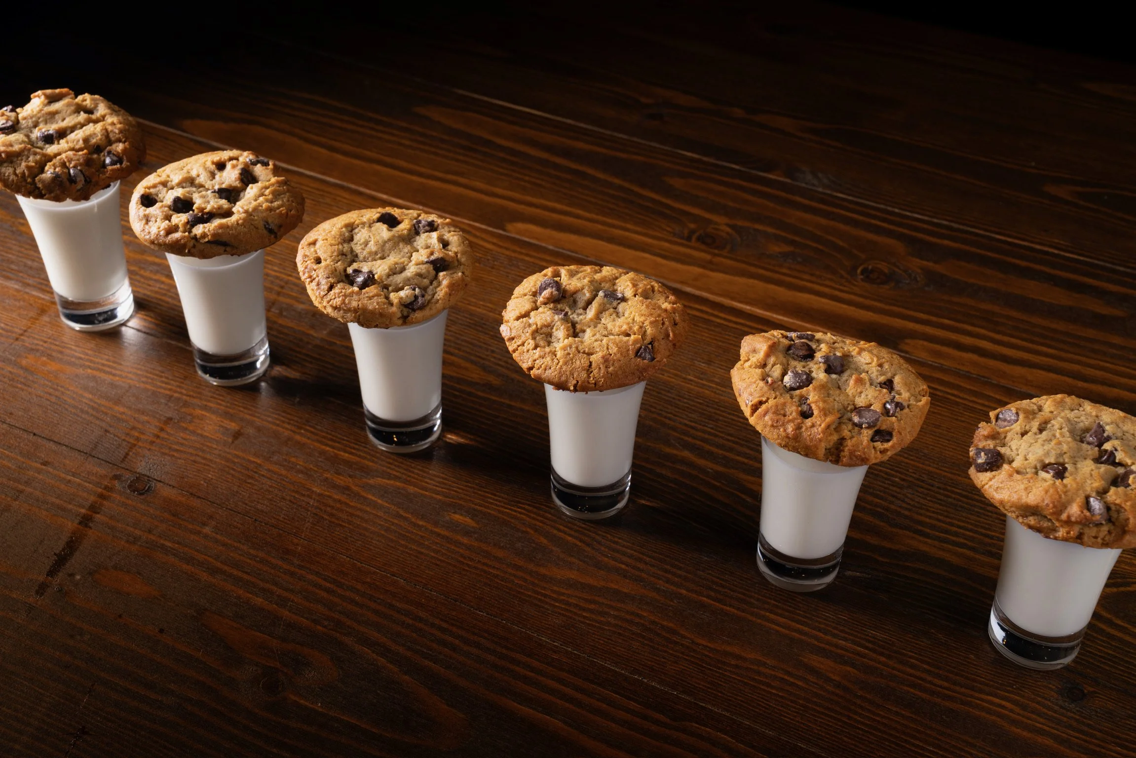 A silver platter with six chocolate chip cookies and dollops of white chocolate on a dark wooden surface.