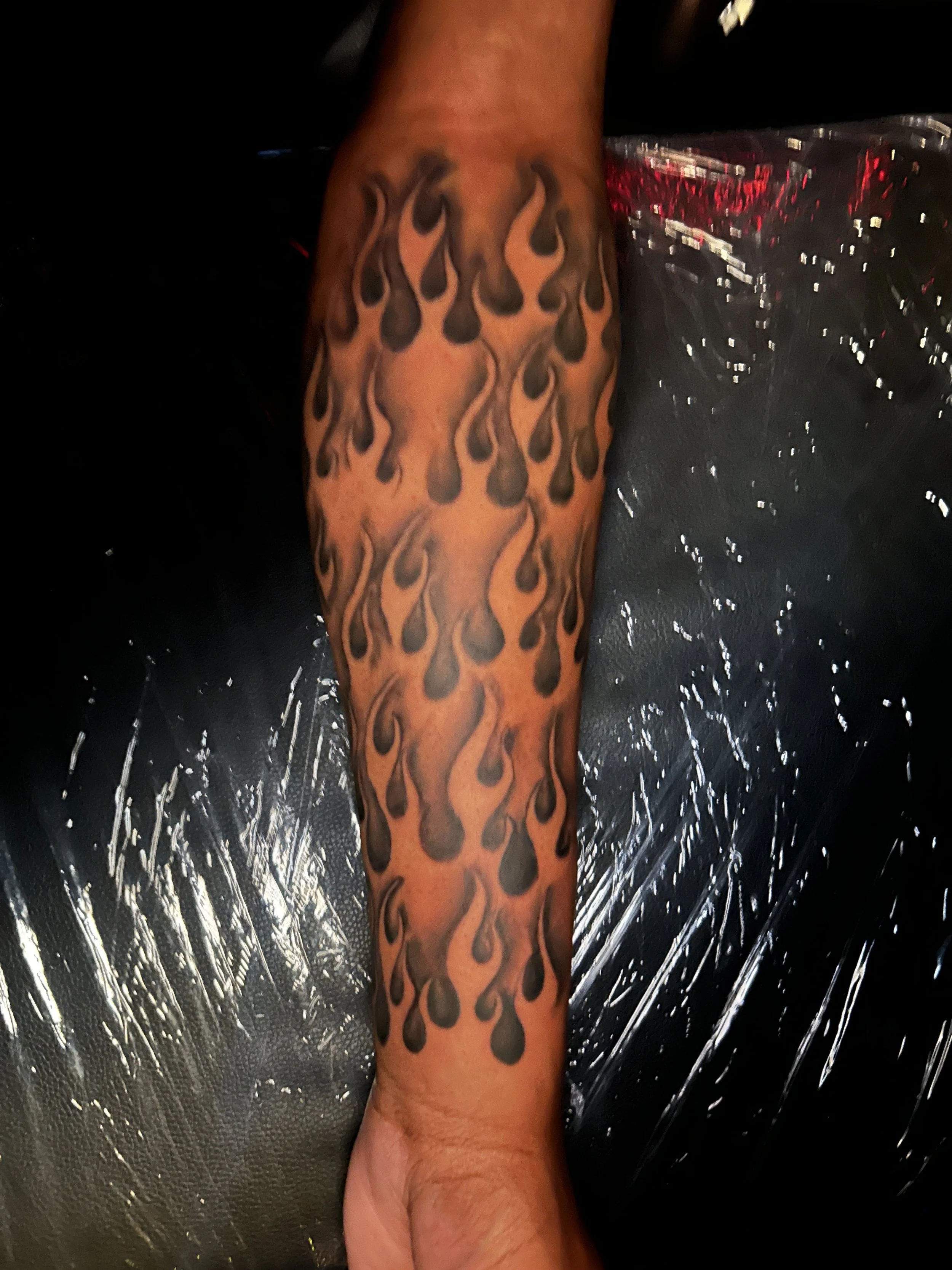 Tattooed forearm with black flame-like flames patterned design.