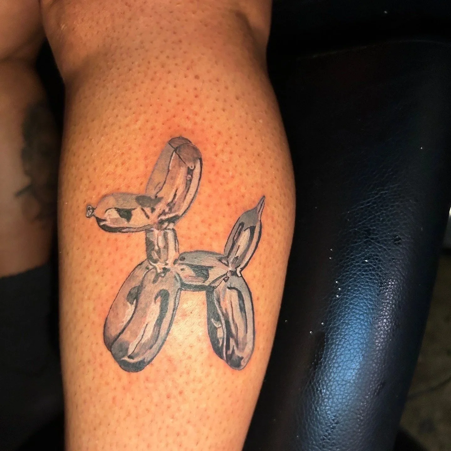 Tattoo of a balloon animal in the shape of a dog on a person's leg.