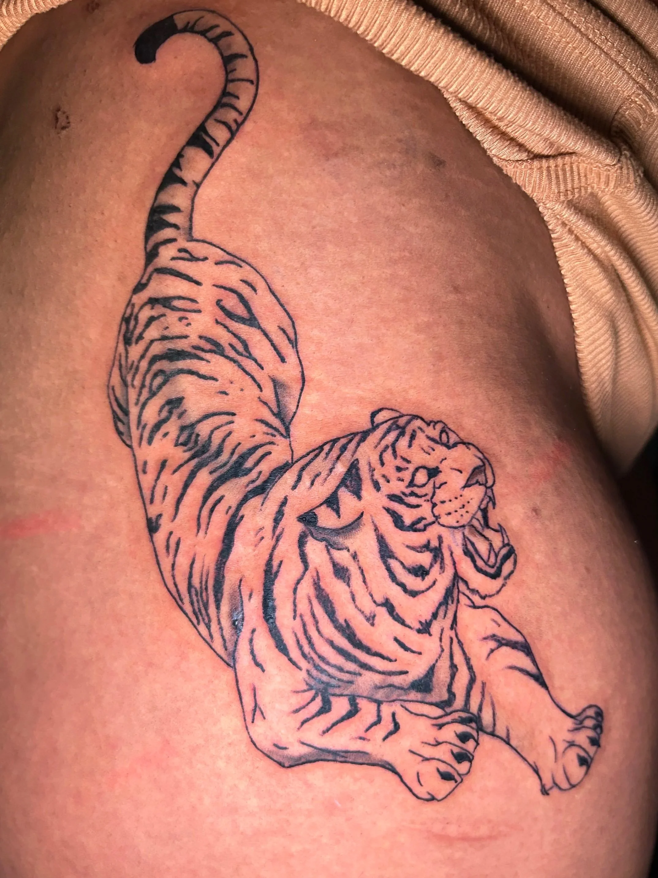 Tattoo of a leaping tiger with bold black outline on person's upper arm.