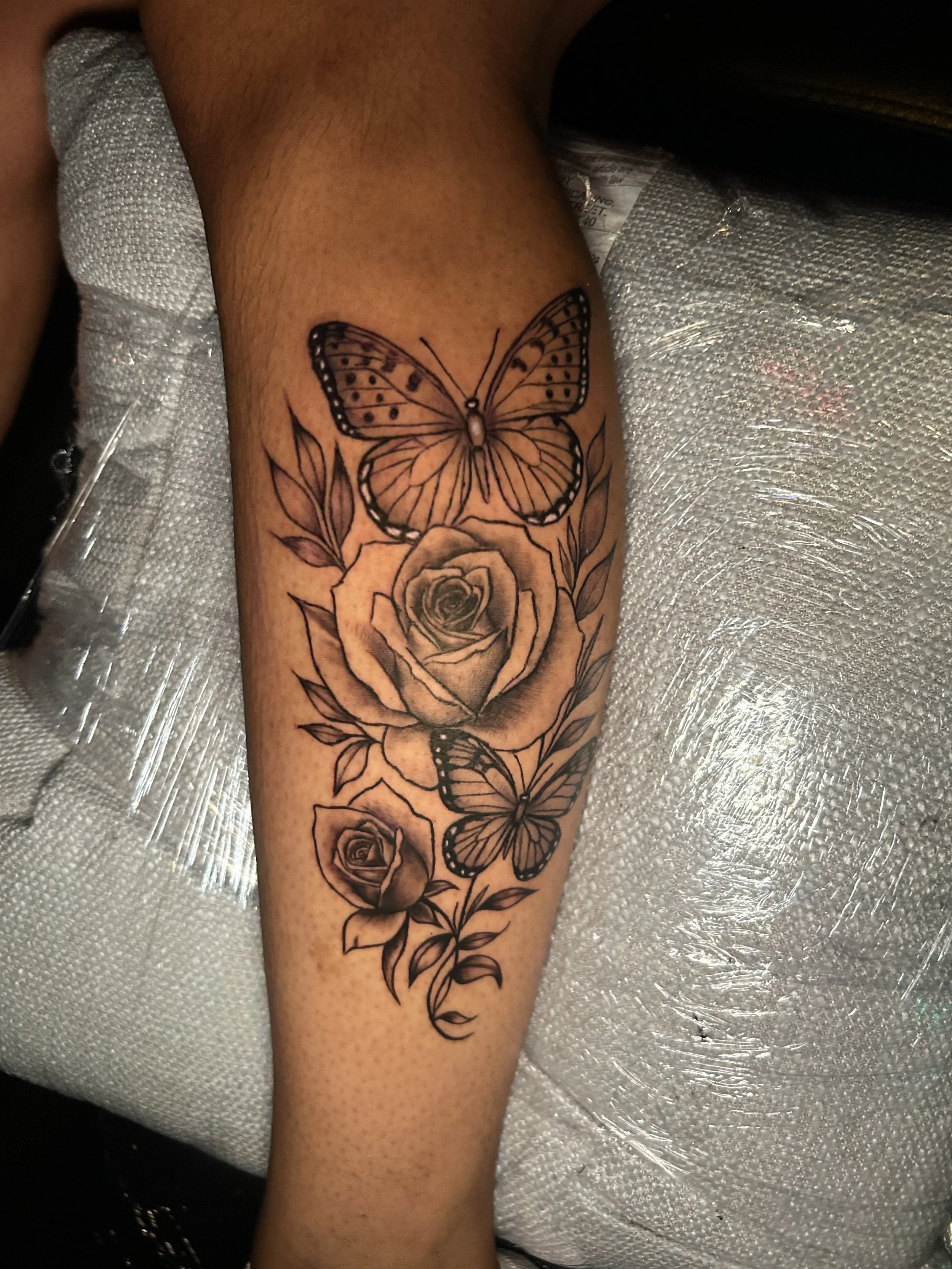 Tattoo of a butterfly, roses, and leaves on a person's forearm.