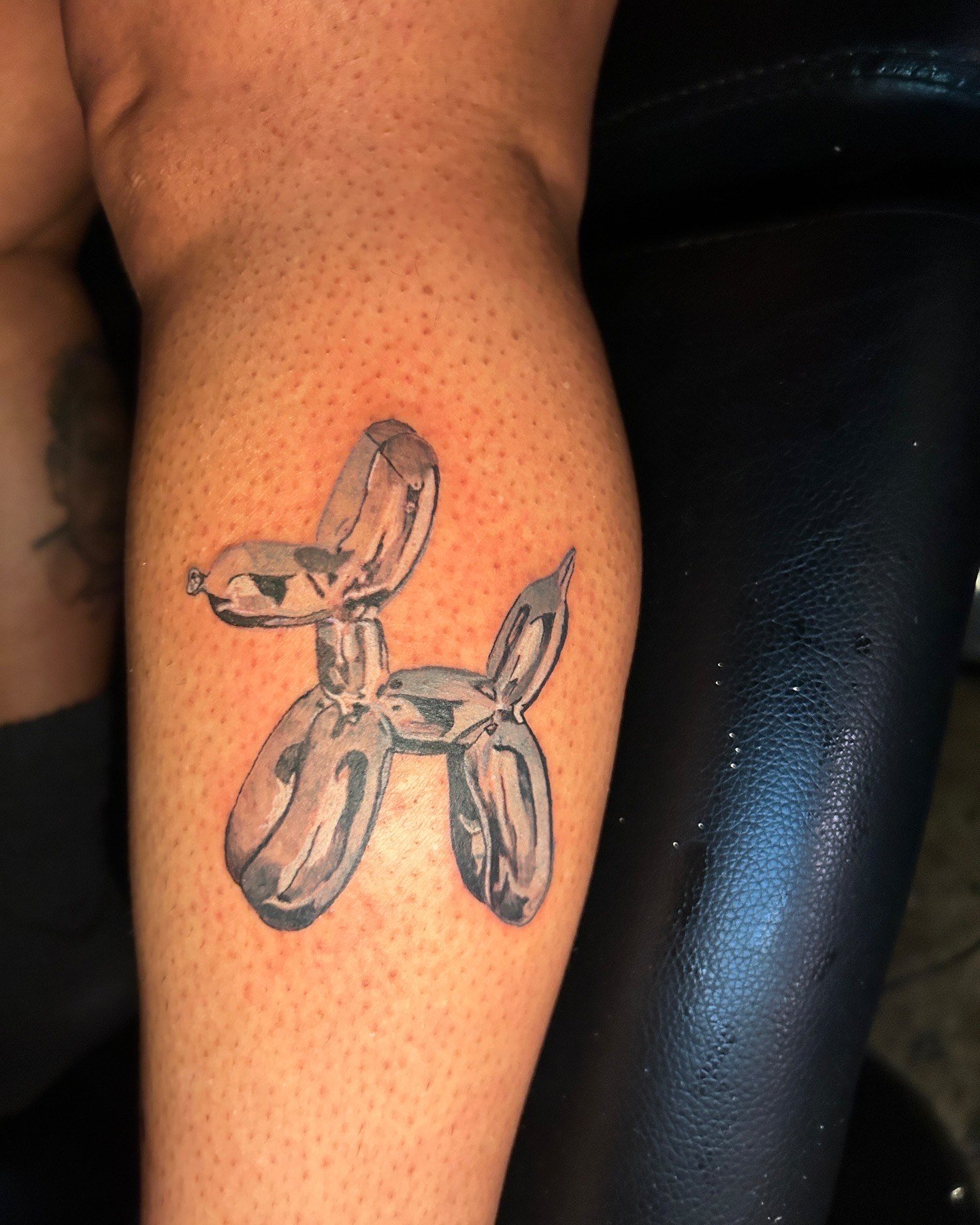 Tattoo of a balloon animal dog on person's arm.