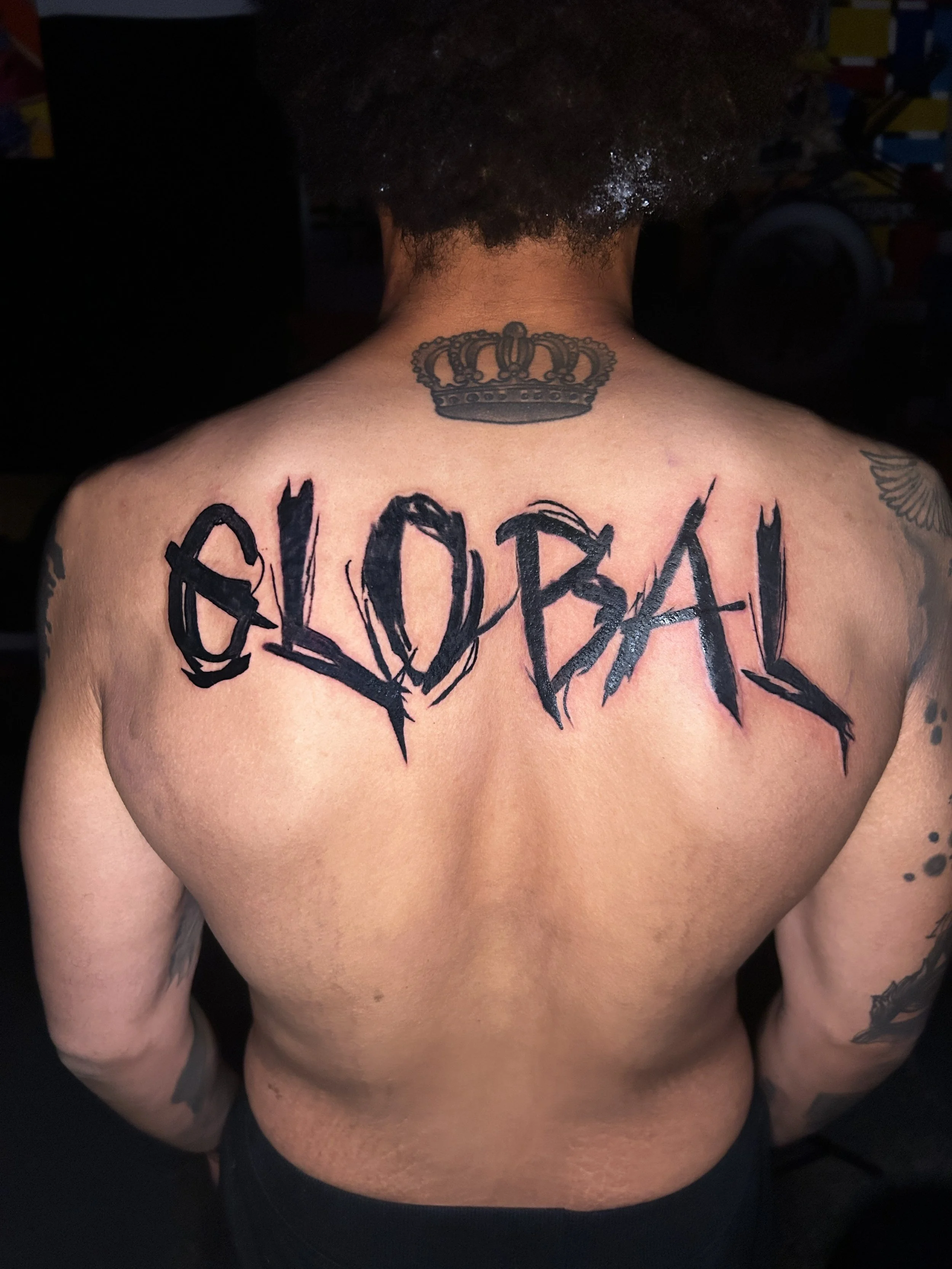 A person's back with a tattoo of the word 'GLobal' in bold, black, graffiti-style letters, and a crown tattoo above the word.