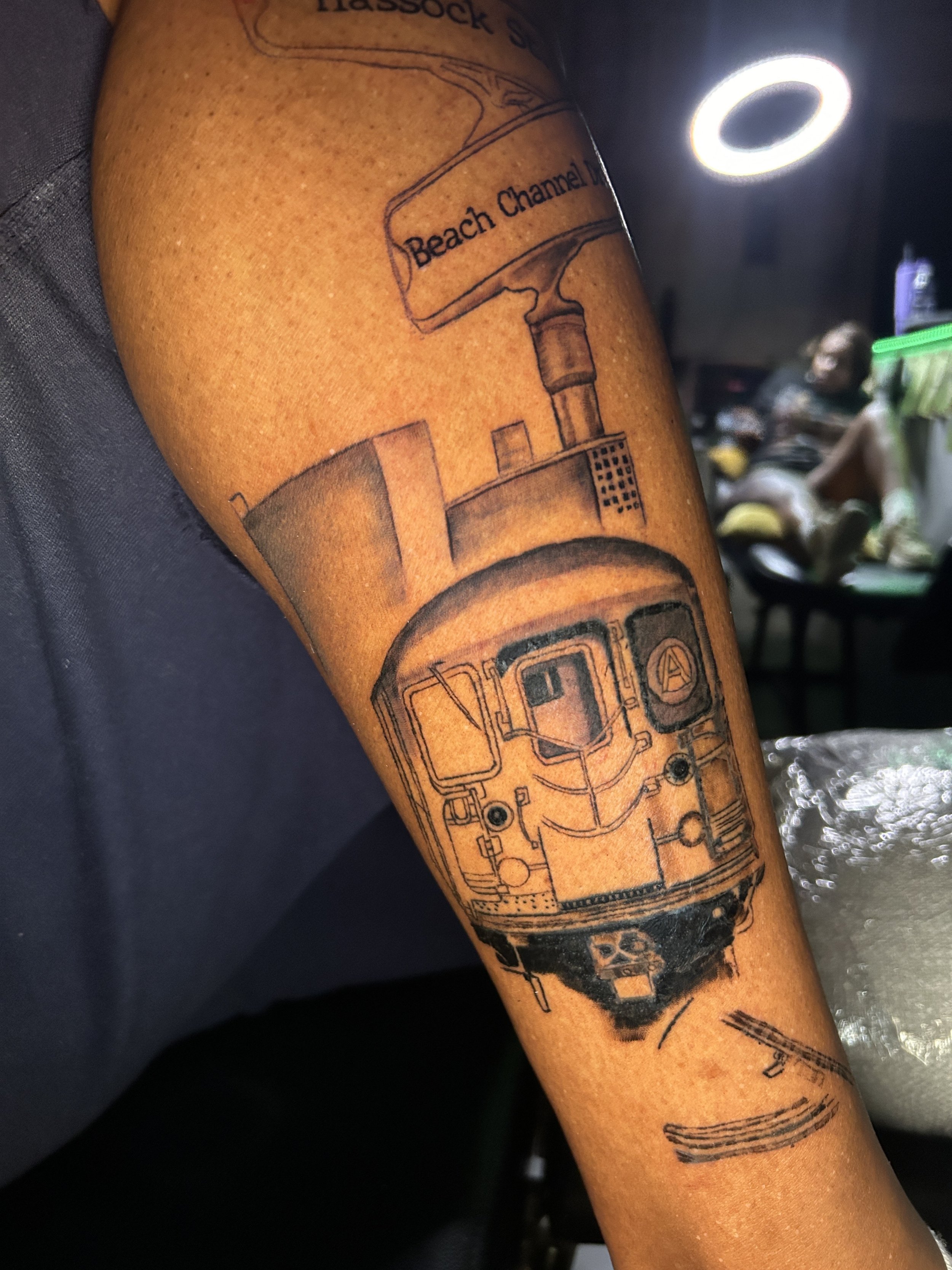 Tattoo of a train and a water tower with the words 'Beach Channel' on the water tower on a person's forearm.