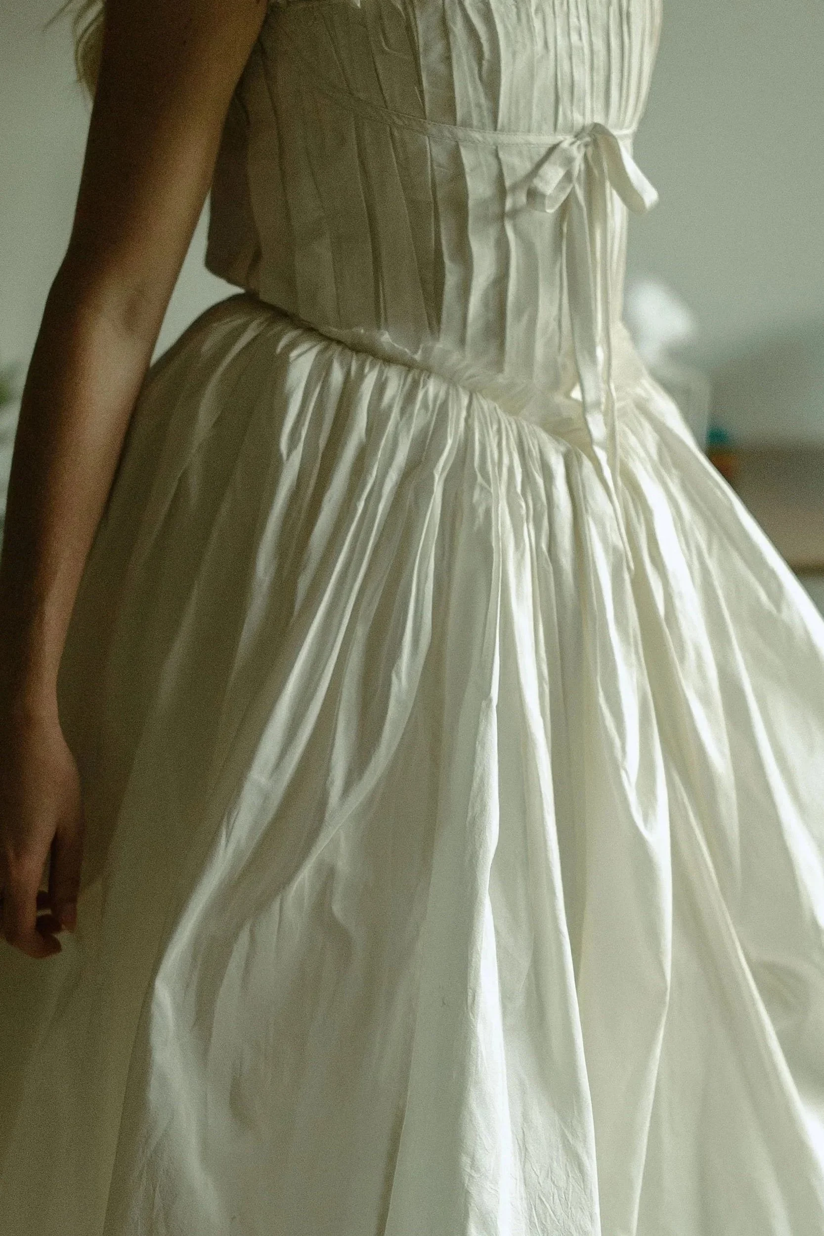 Part of a woman wearing a vintage ivory wedding dress with a satin bodice and full pleated skirt. Documented by destination documentary videographer.