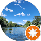 Scenic view of a river surrounded by lush green trees under a blue sky with scattered clouds.