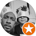 A man and a young boy in close-up, both wearing hats, with the man looking at the camera and the boy smiling. Background shows other people.