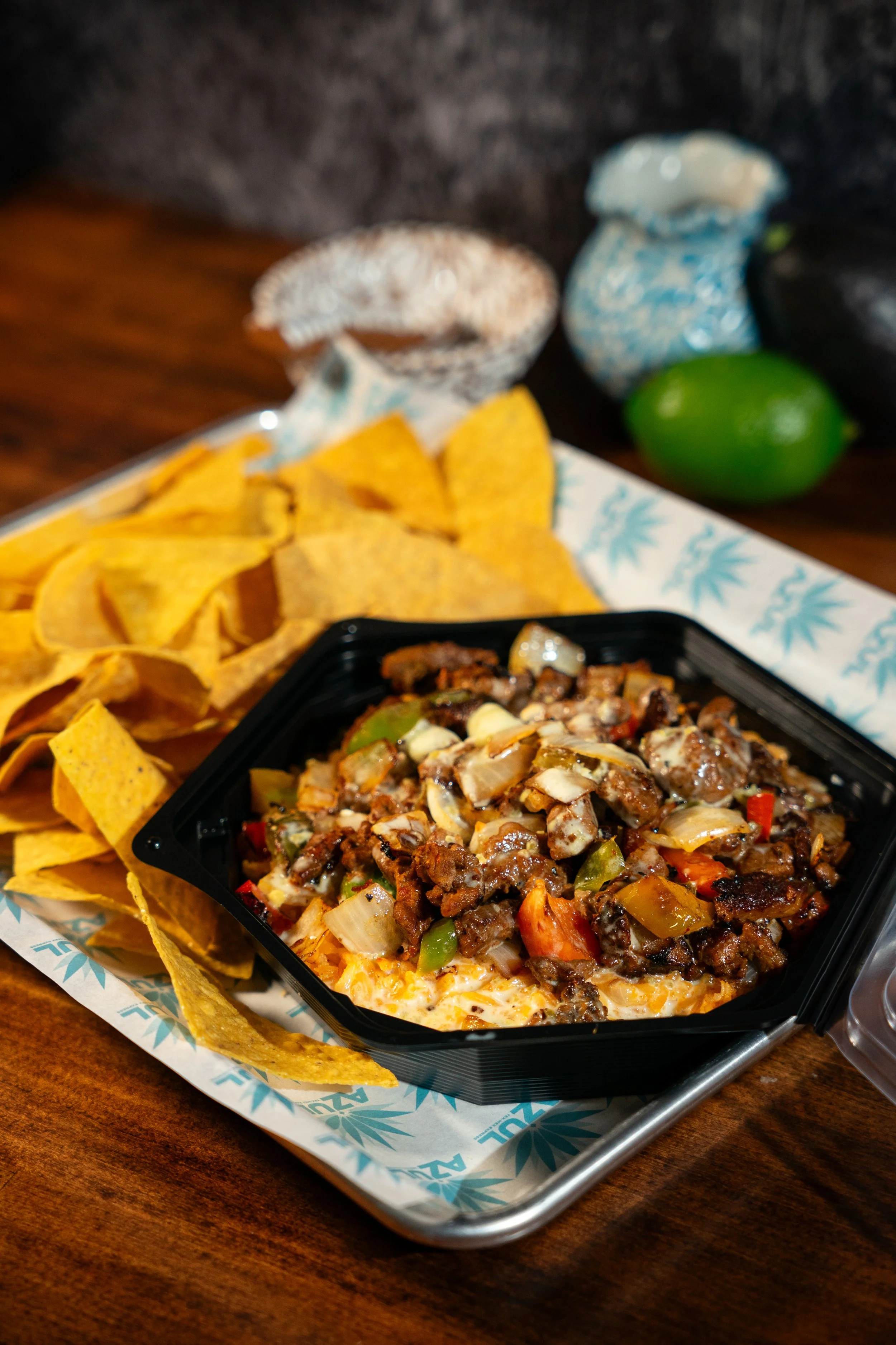 Bowl of beef nachos with vegetables and chips on a tray.
